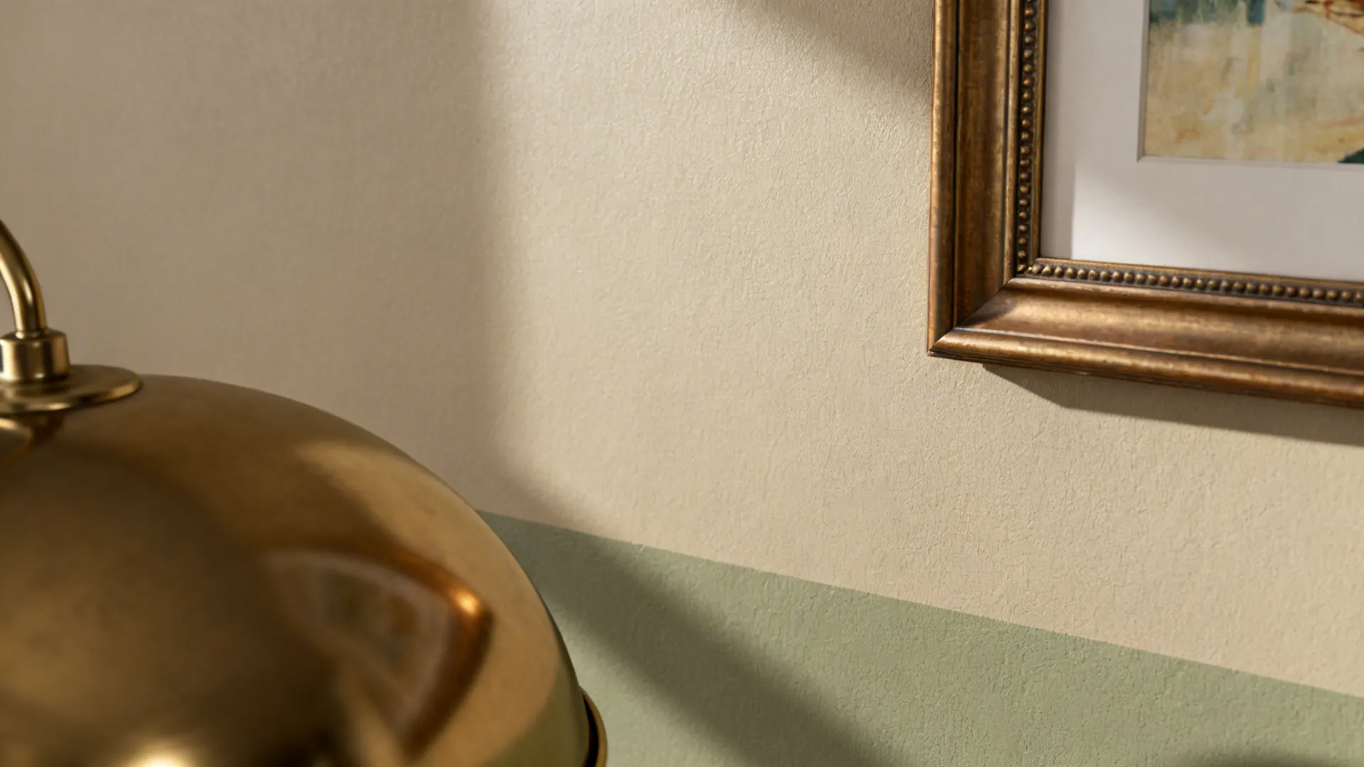Macro of greige and sage wall paint with satin brass lamp and frame detail.