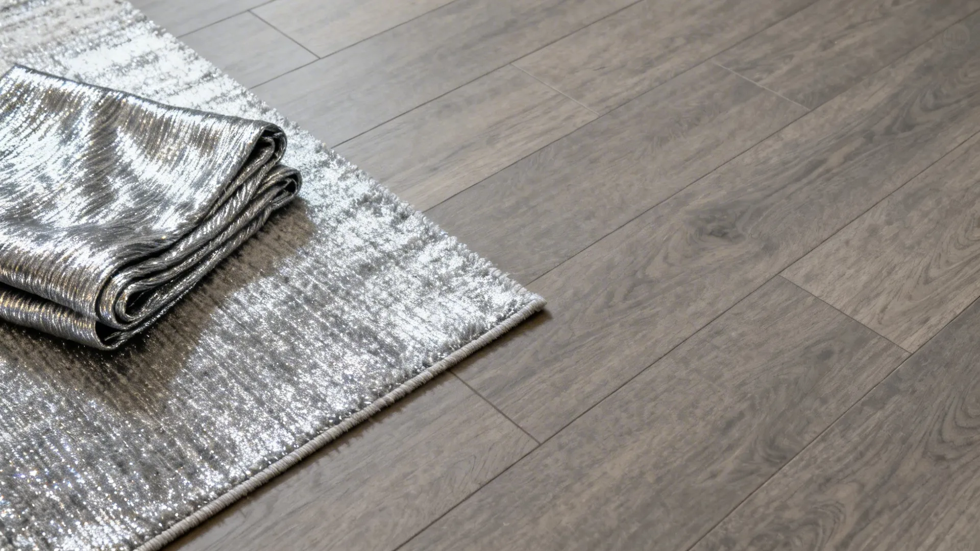 Top-down view of warm grey flooring layered with a silver-toned rug and metallic-thread throw.