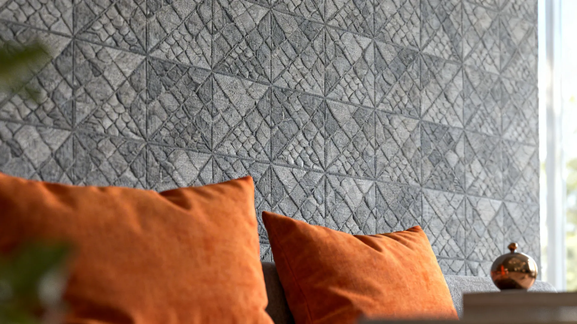 Close-up of grey geometric wallpaper paired with warm orange cushions in a small living area.