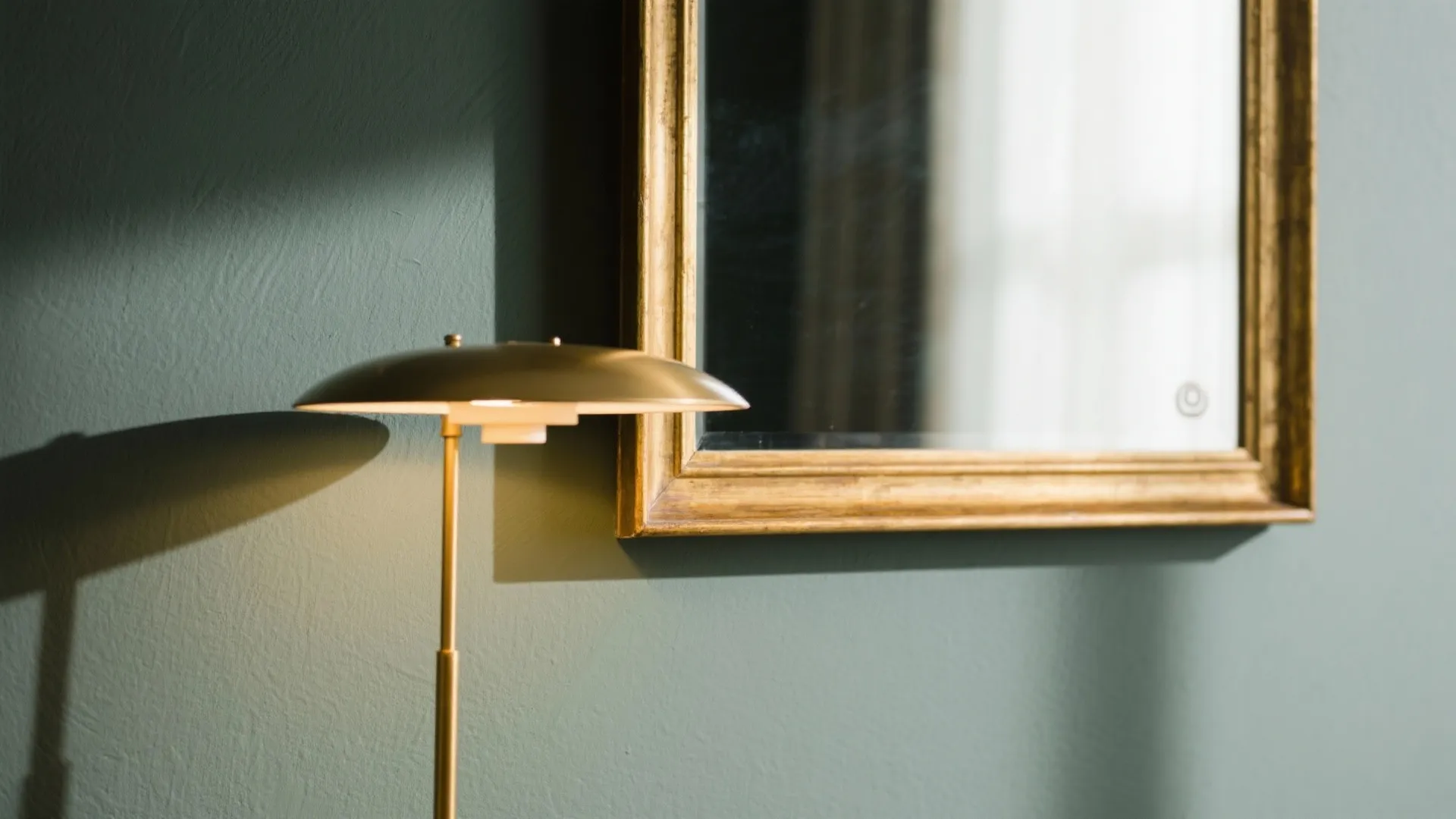 Close up of gold floor lamp and mirror with gold frame against dark green wall