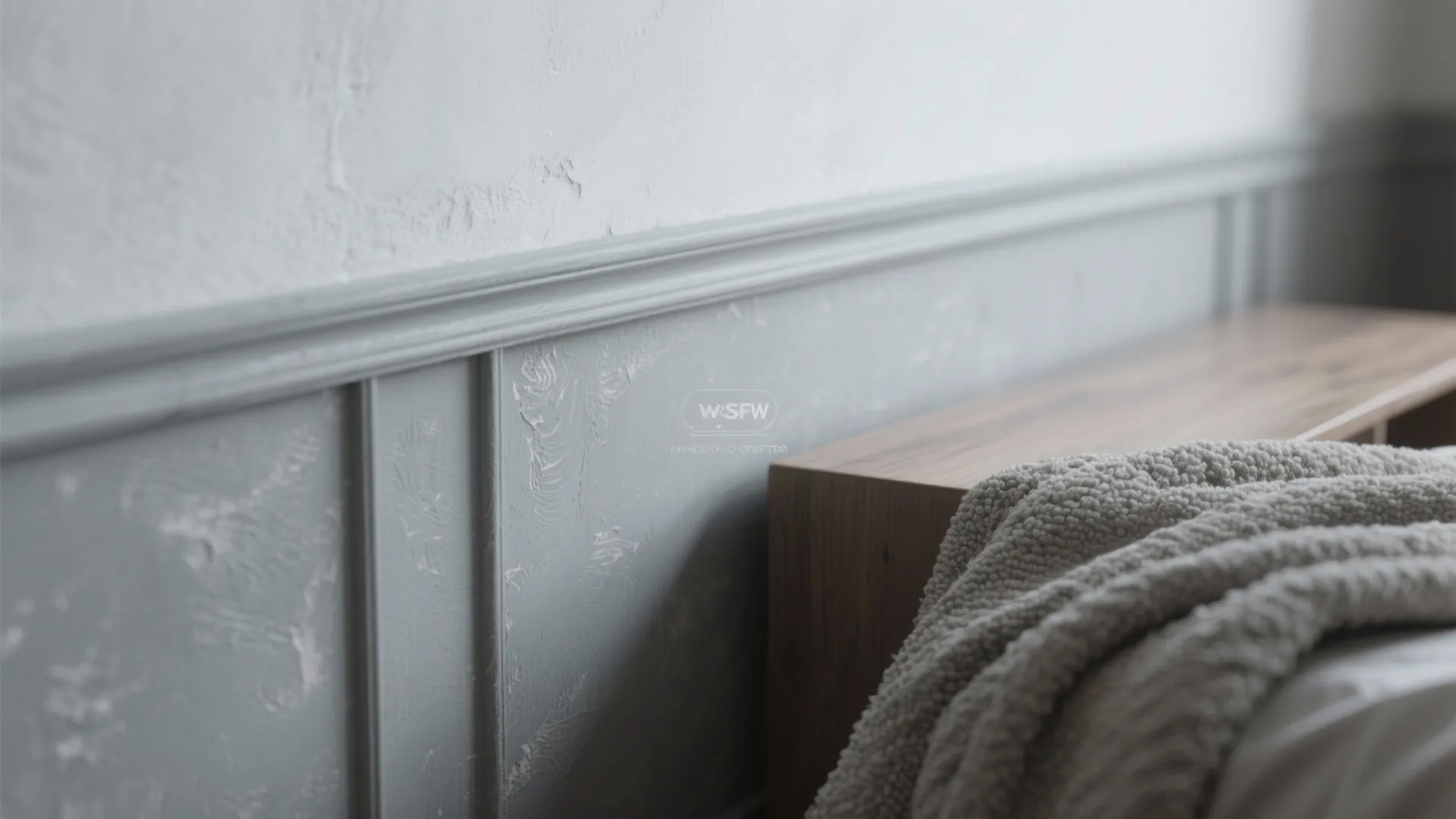 Close up view of grey textured wall panel next to a wooden cabinet and blanket