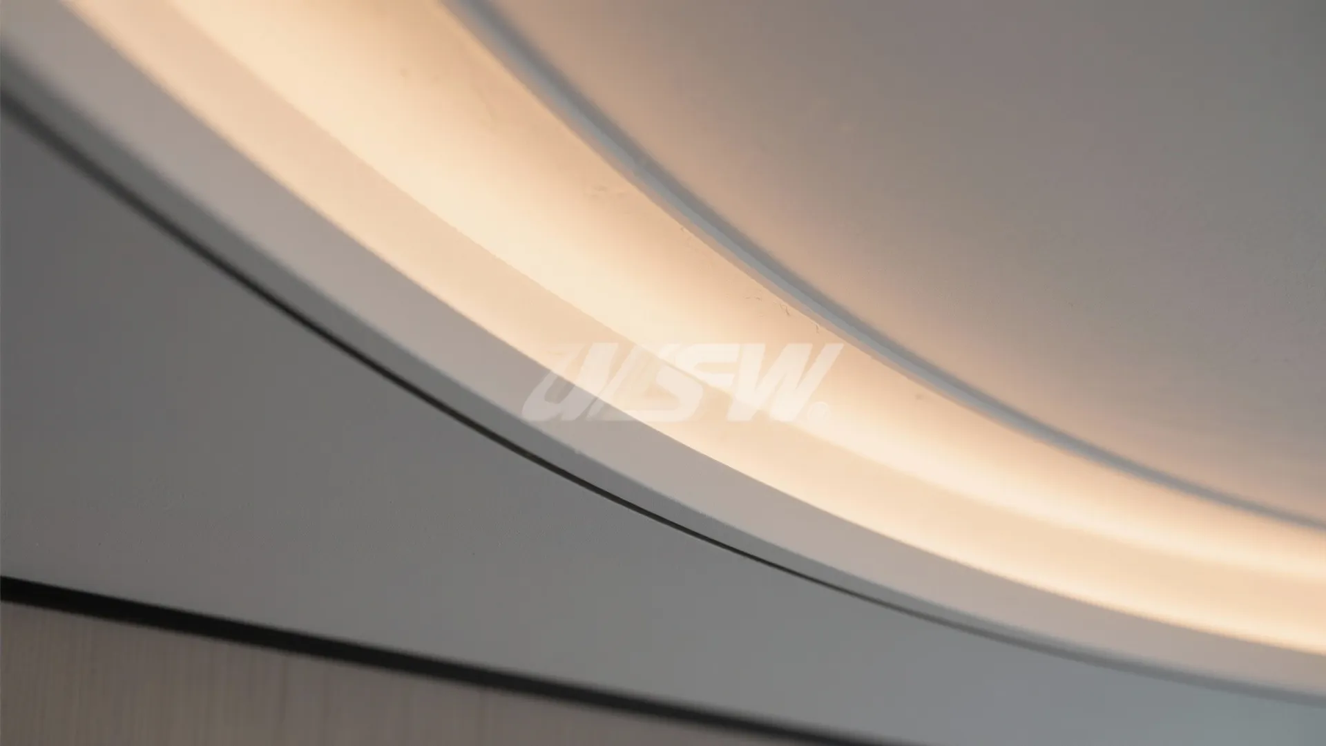Macro of curved gypsum ceiling with warm perimeter LED halo showing crisp edge and smooth finish.