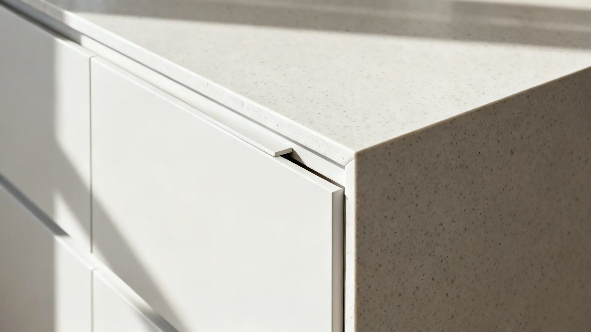 Close-up of a matte white handleless drawer and toe-kick seam on a minimalist L-shaped island.