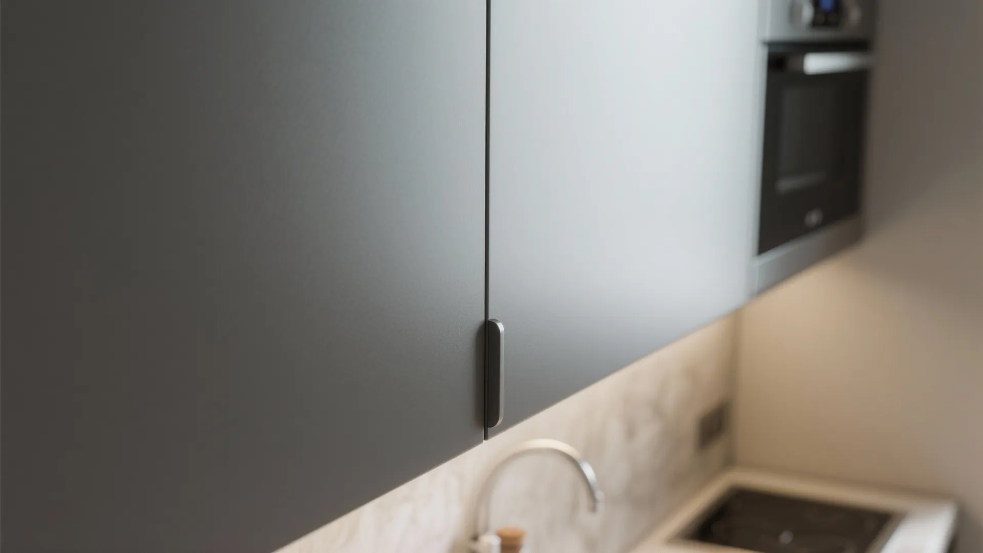 Close up of grey kitchen cabinet doors with a small black handle above a white countertop