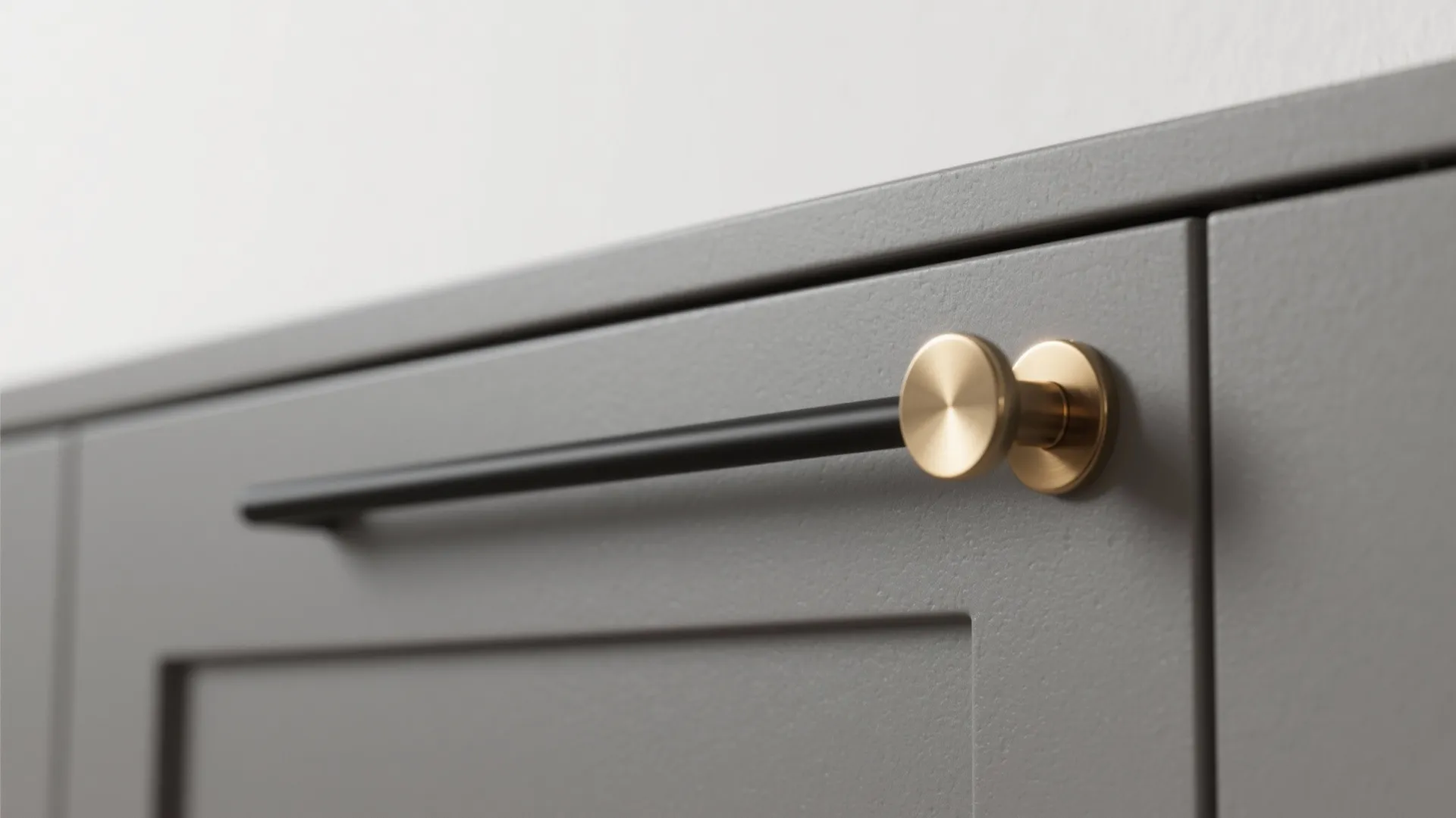 Close up of grey cabinet door with modern round gold handle and black metal pull bar