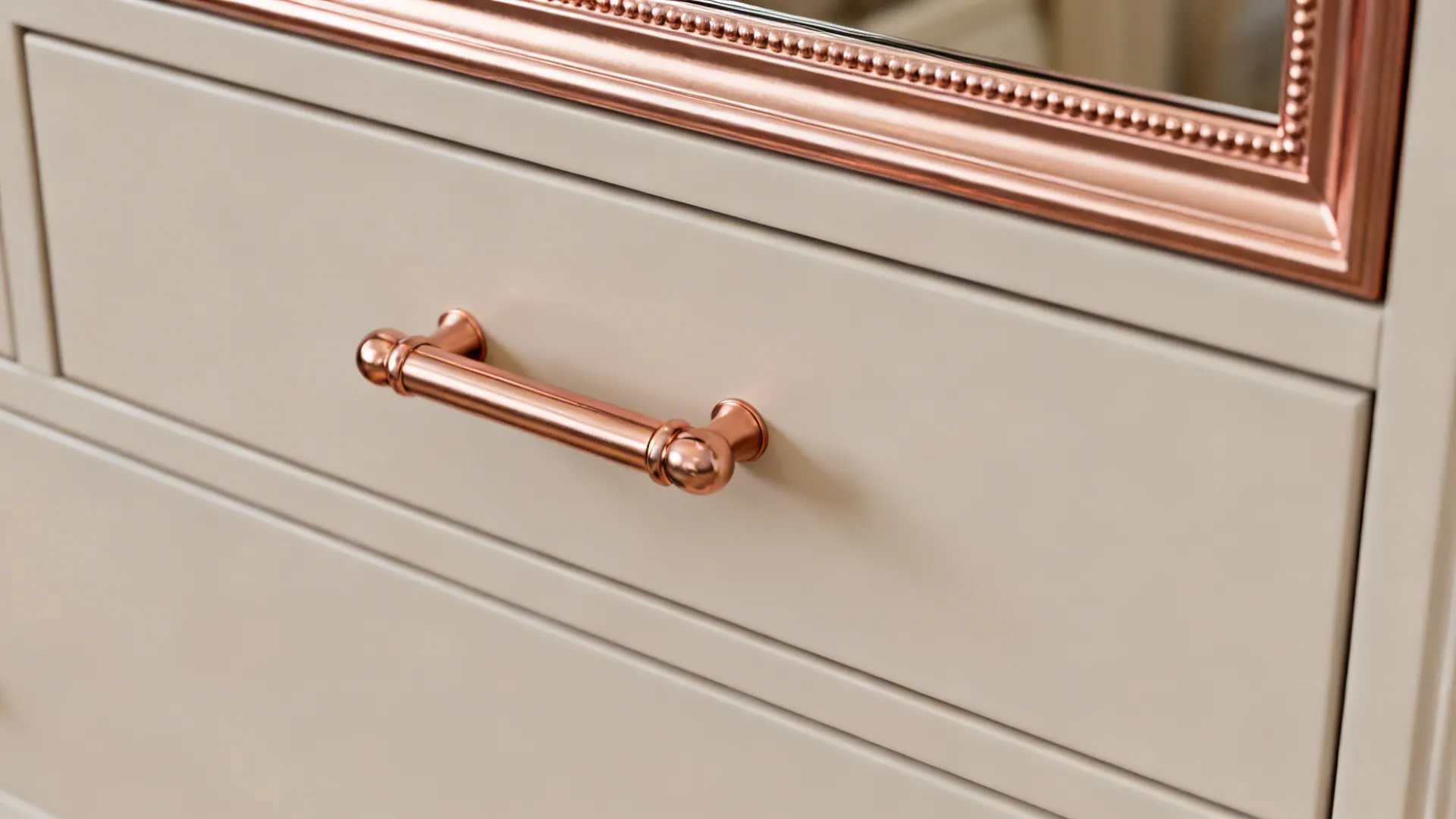 Close-up of rose gold drawer pull and mirror frame on a matte cabinet showing finish detail
