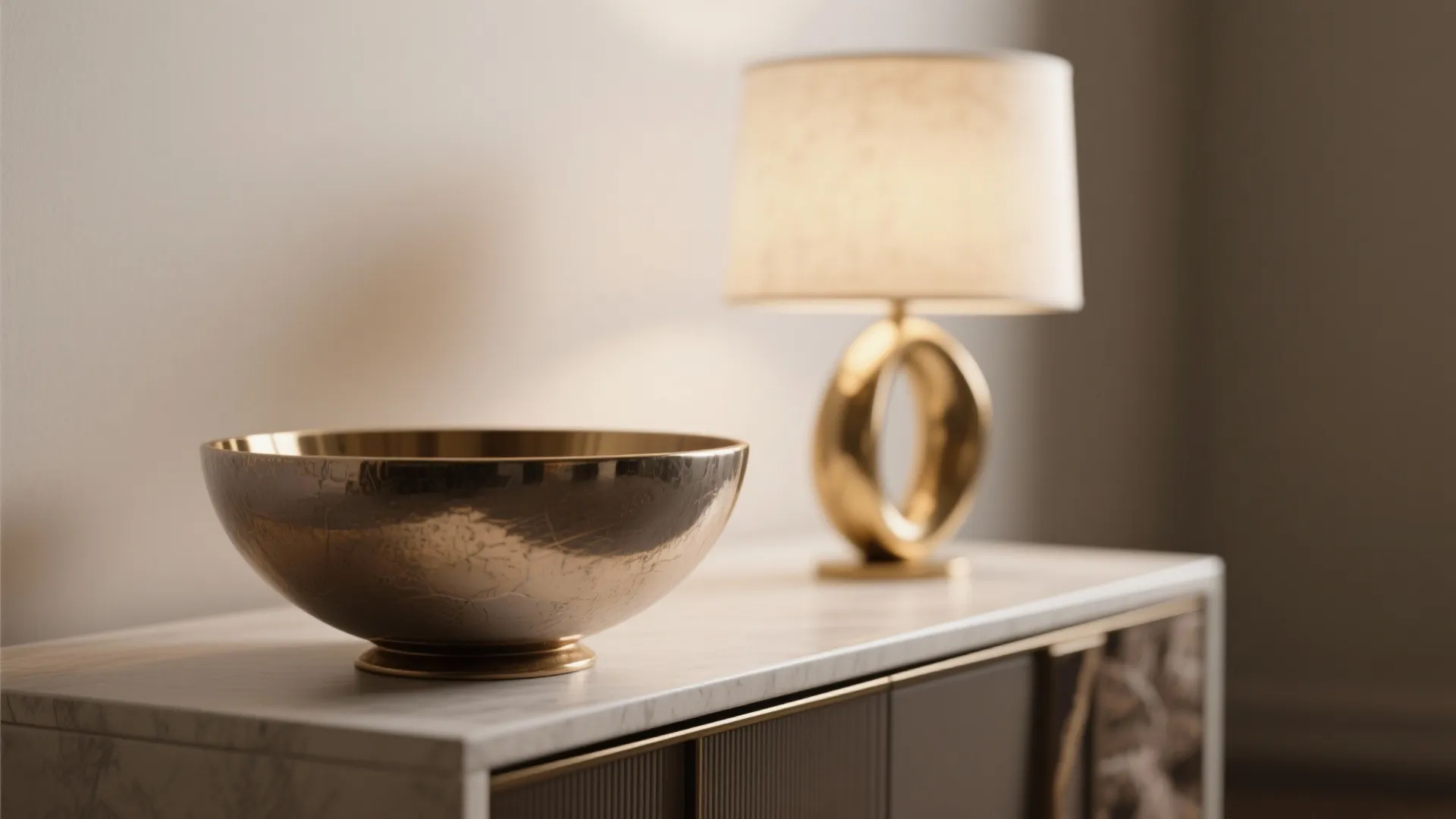 Large gold bowl on marble cabinet with a modern table lamp and soft warm lighting