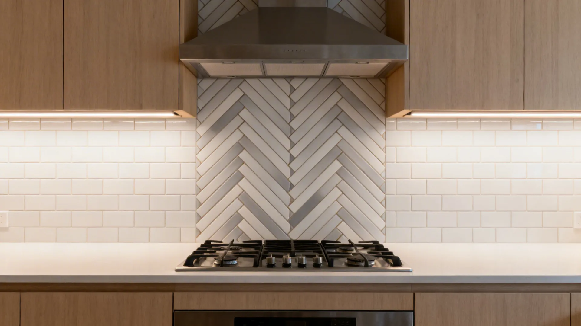 Neutral herringbone tile backsplash centered on the cooktop in a compact kitchen.
