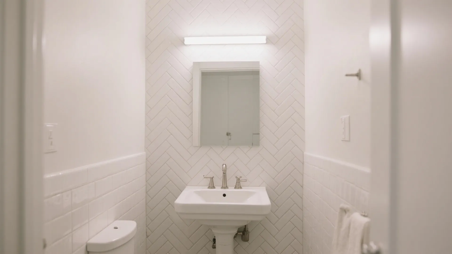 Small white bathroom showing sink mirror toilet wall light and classic herringbone pattern wall tile design