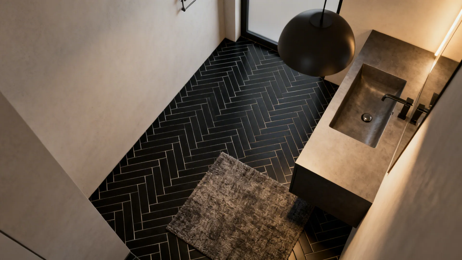 Small ensuite featuring a luxurious black herringbone tile floor and floating vanity under warm lighting.