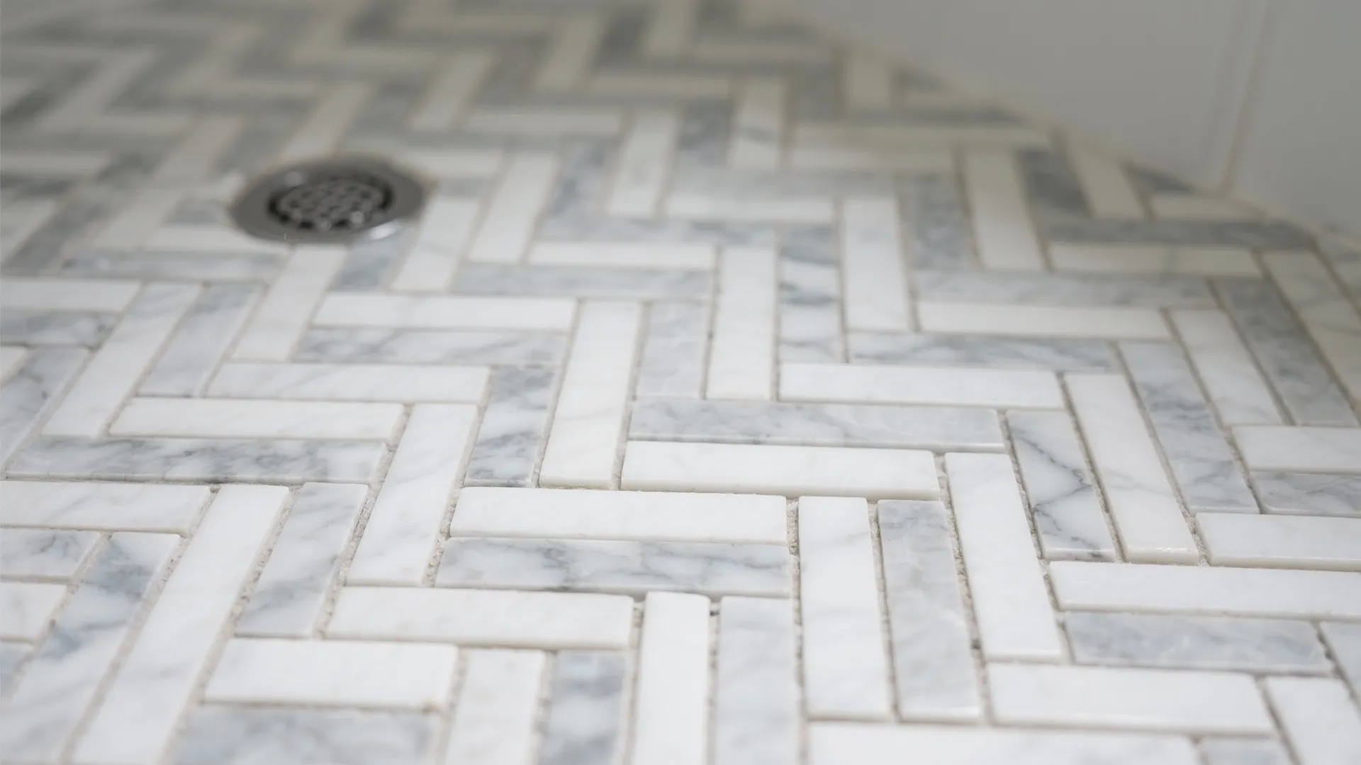 Macro of herringbone marble mosaic with light gray grout for traction and detail.