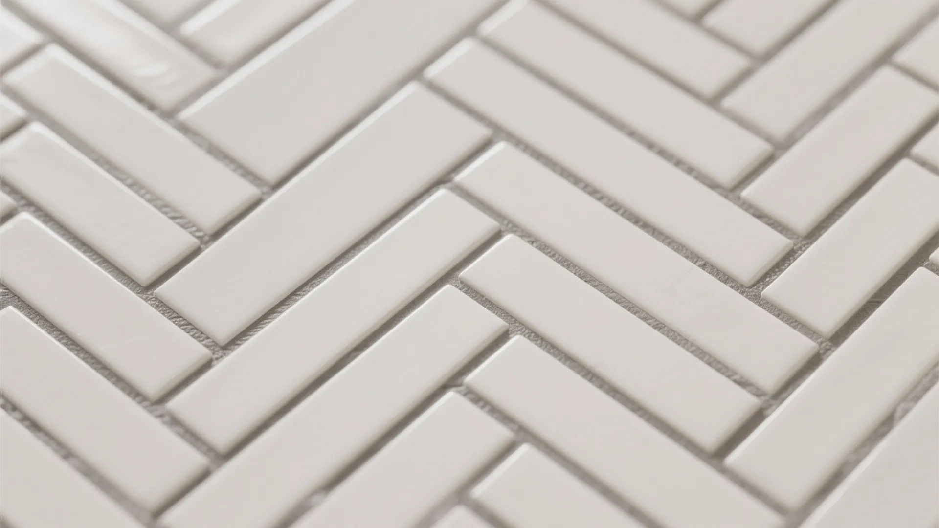 Close-up of off-white ceramic tiles in herringbone with warm gray grout, showing crisp diagonal lines and refined texture.