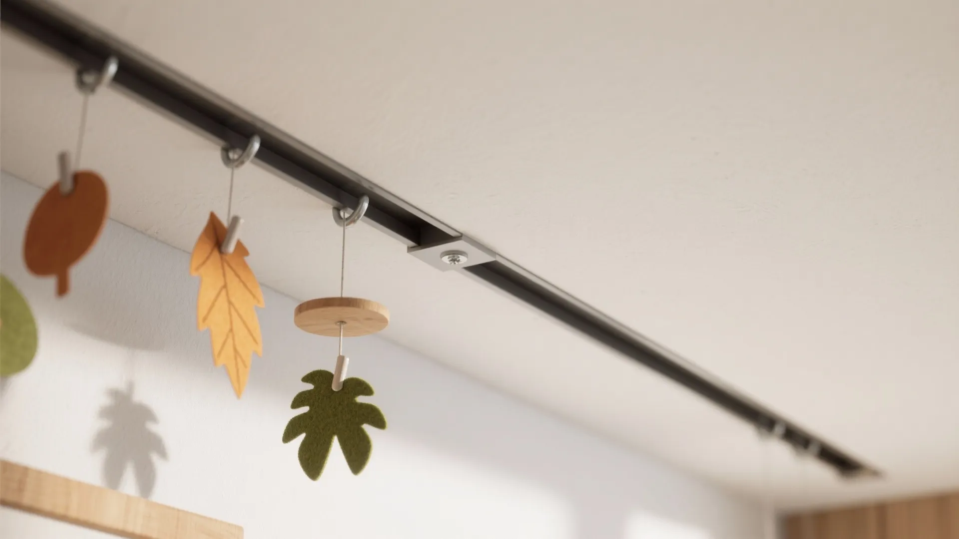 Metal art hanging rail mounted on white ceiling with several colorful decorative felt leaf shapes