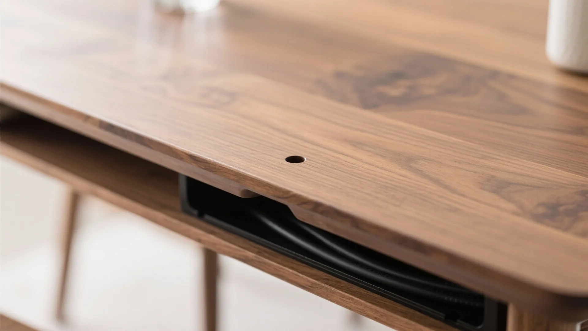 Close up of a wooden desk with a small hole for managing hidden power cables