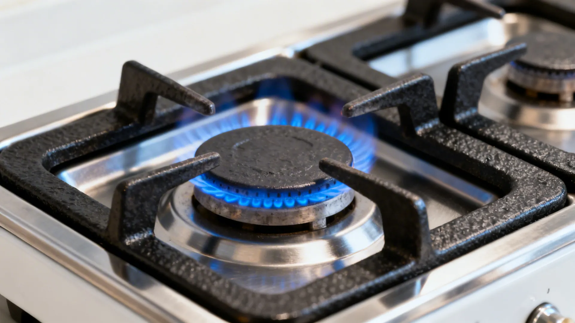Macro of high-BTU gas burner with blue flame and cast-iron grate on a compact cooktop.