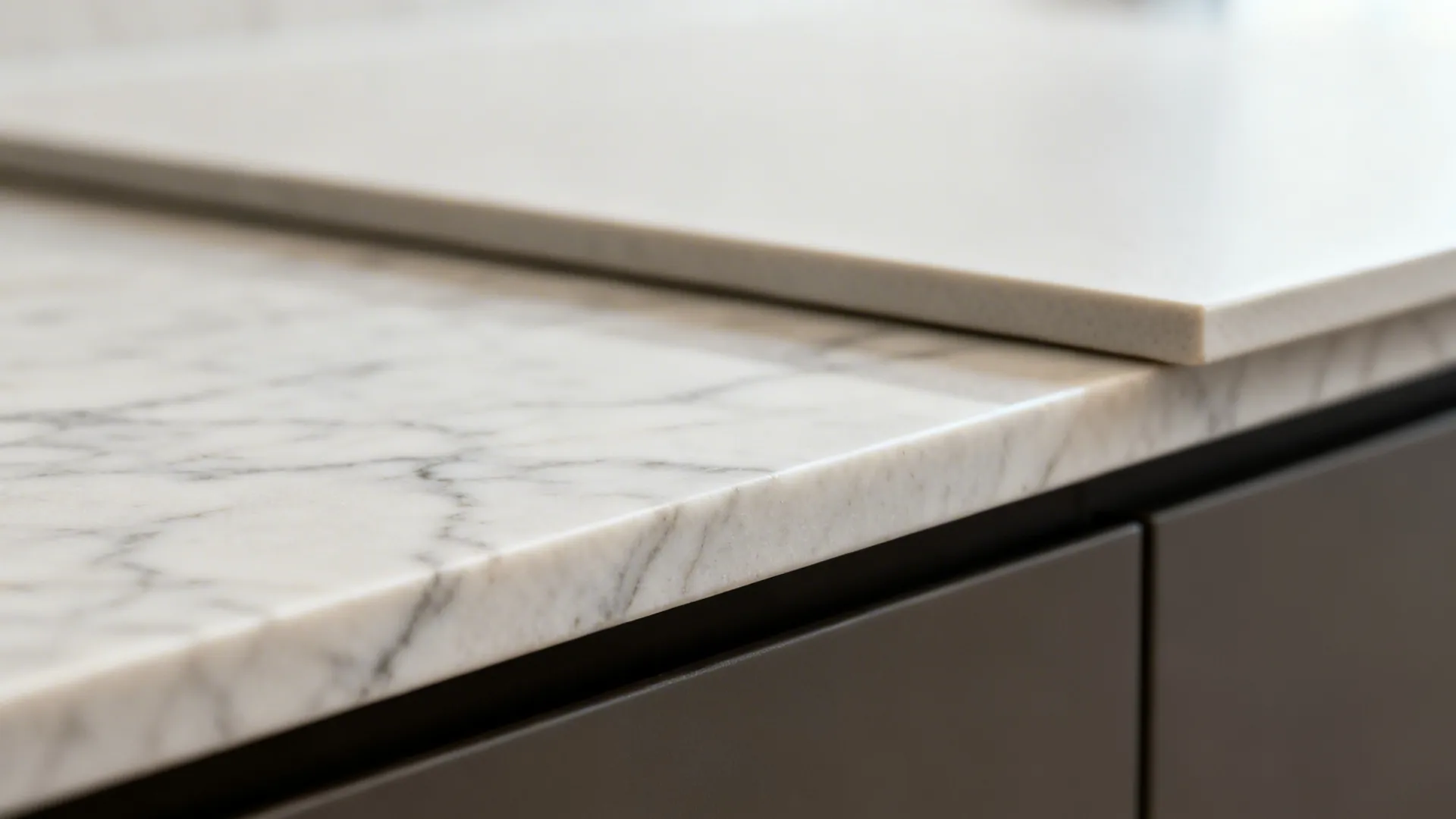 Close up of white marble and beige stone countertop edges on dark grey kitchen cabinet