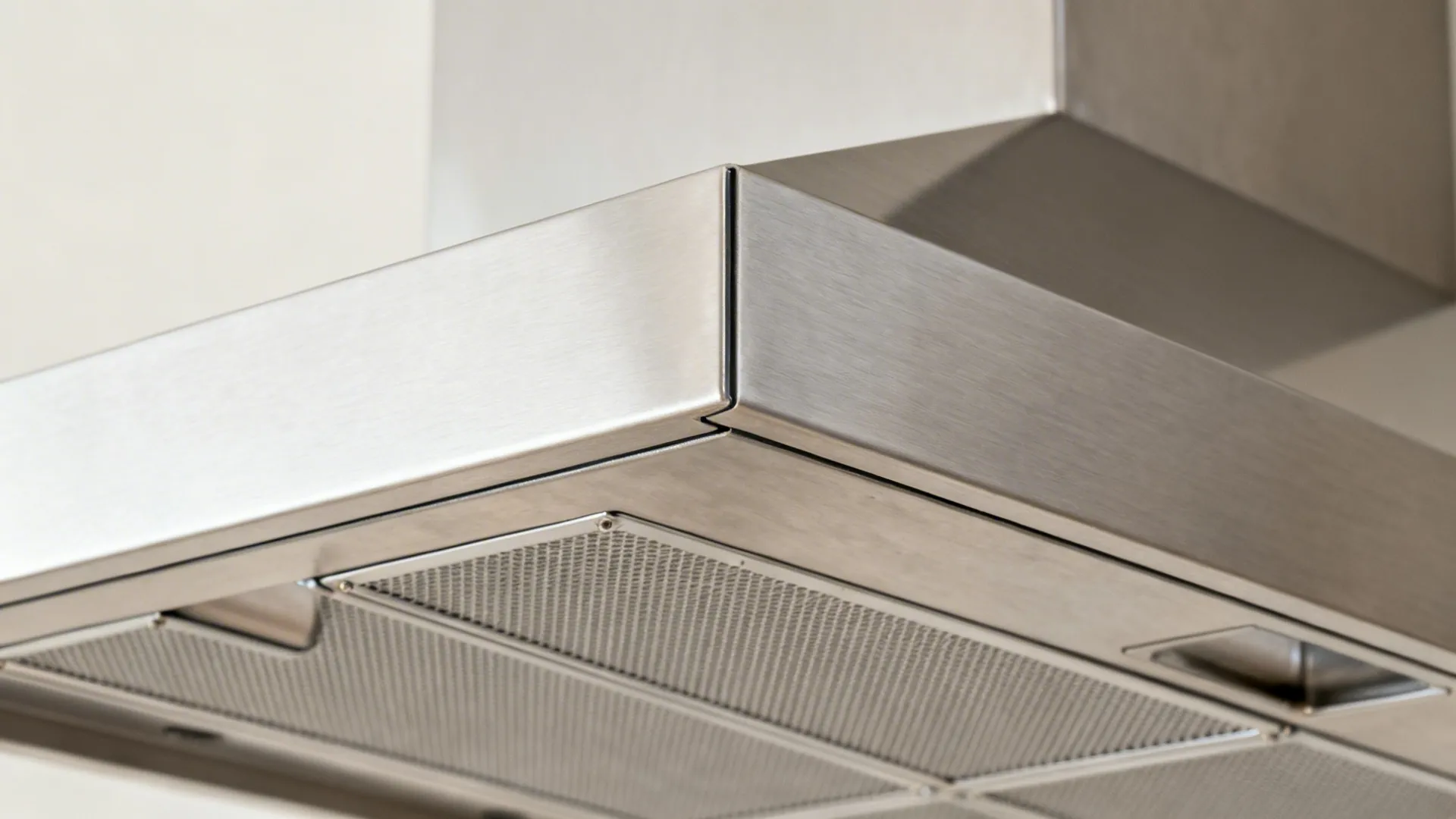 Macro detail of brushed stainless slim hood and metal baffle filter with clean seams.