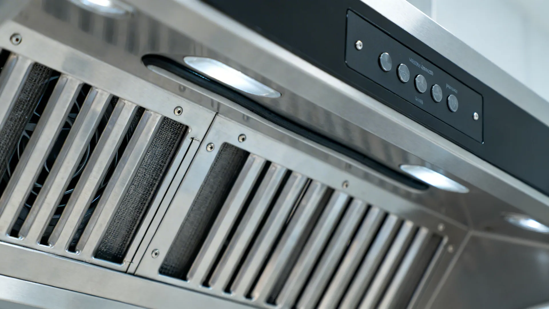 Close up of a stainless steel kitchen vent hood with control buttons and metal mesh filters