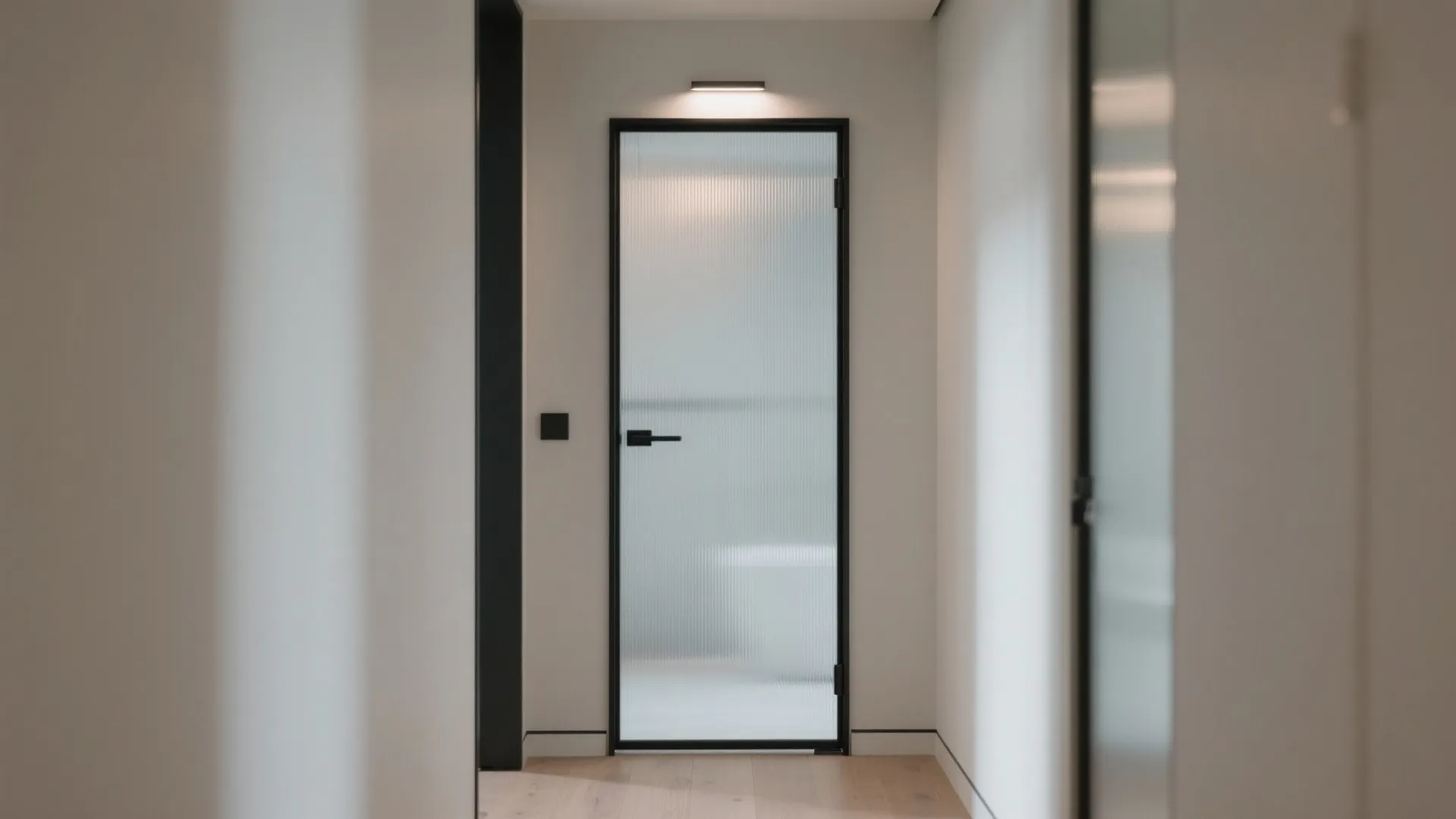 Frosted glass door with black frame positioned at the end of a bright white interior hallway