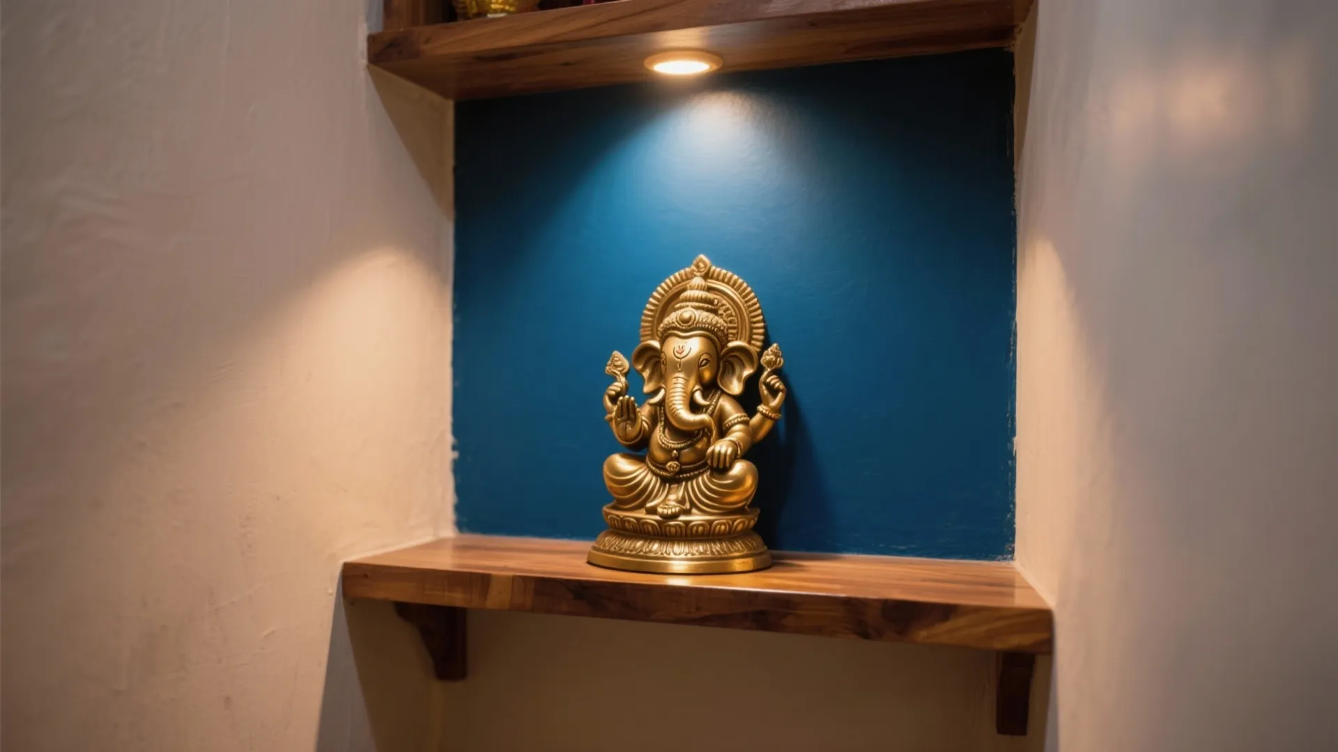 Deep indigo accent wall framing a brass idol on a wooden shelf with warm spotlights.