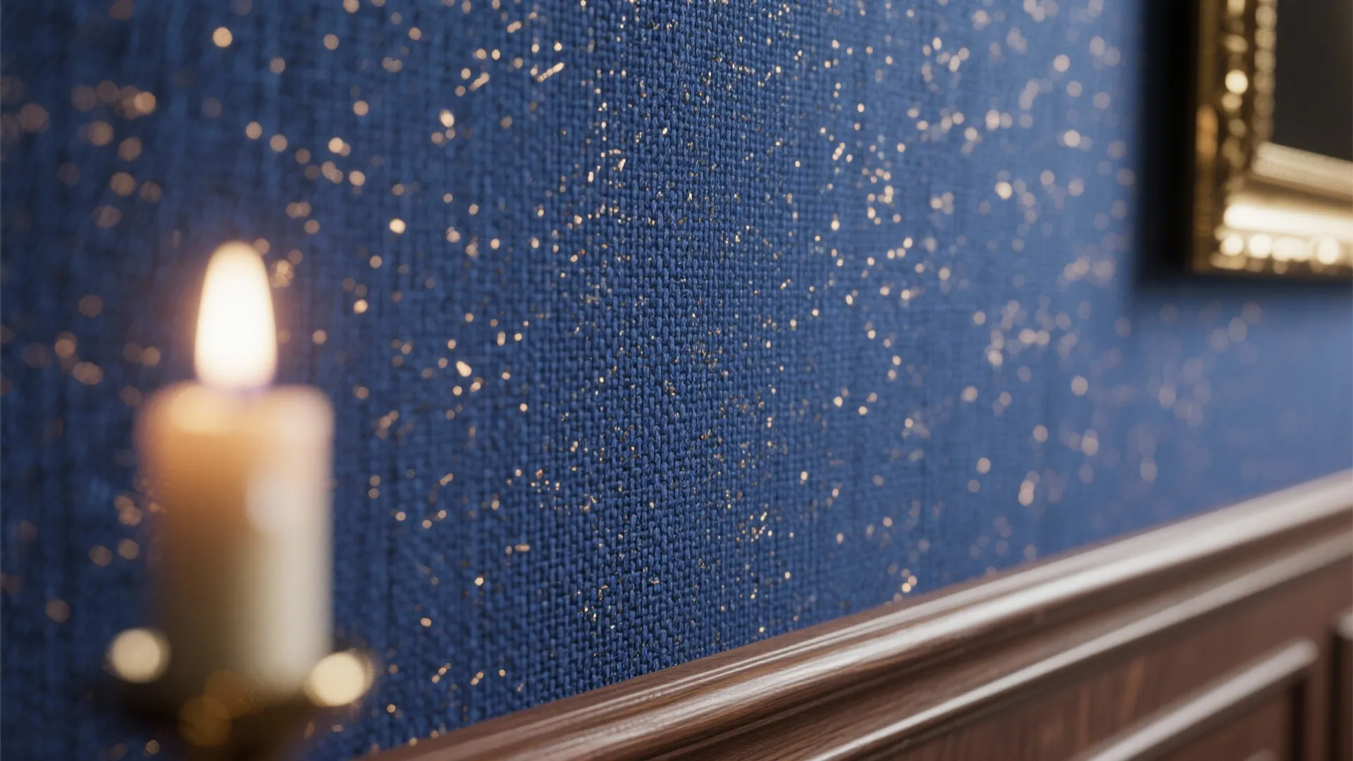 Blue textured wallpaper with gold flecks above a dark wood wall panel and lit candle