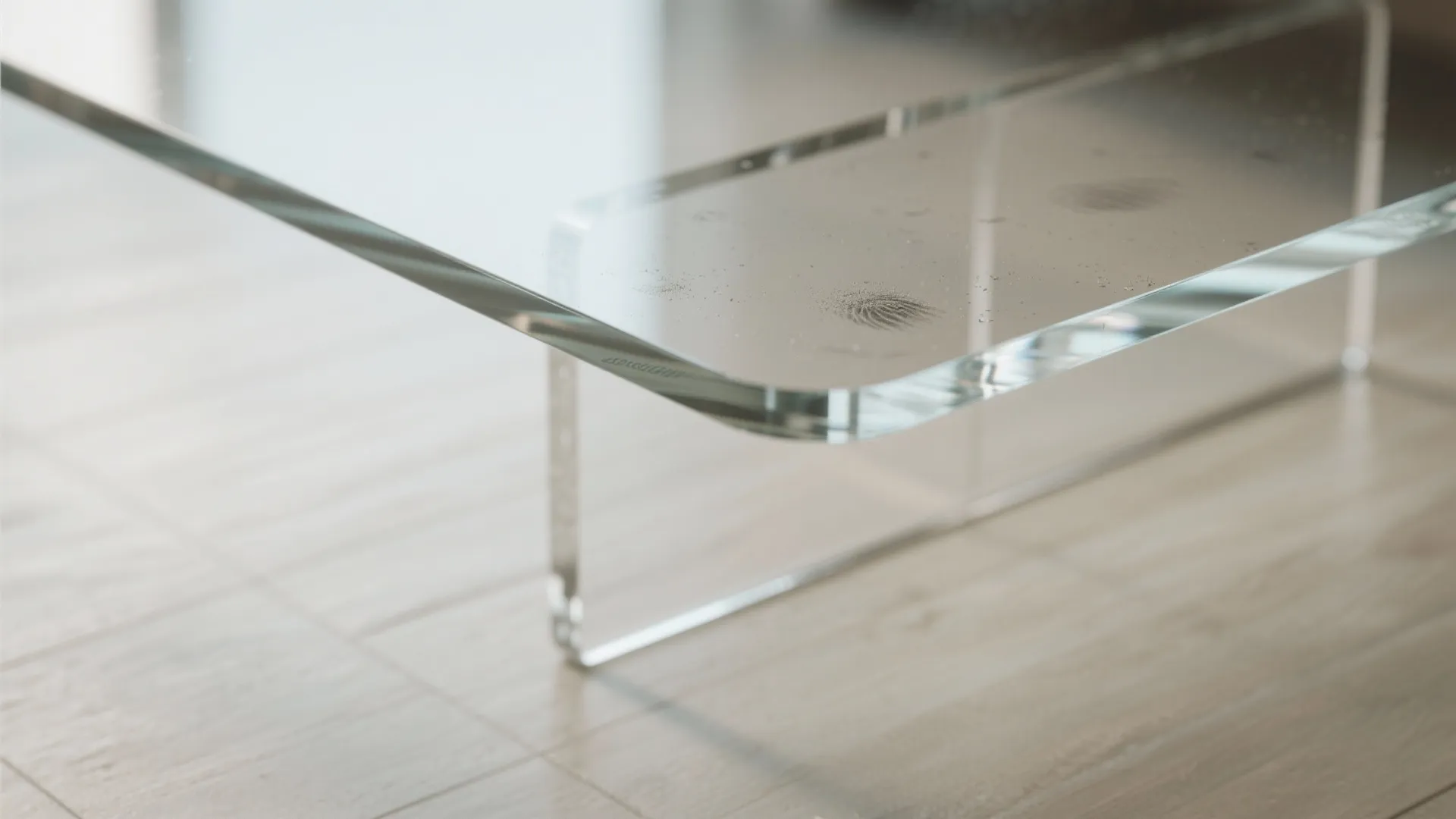 Close up view of a transparent glass table corner showing fingerprints and clear support base design