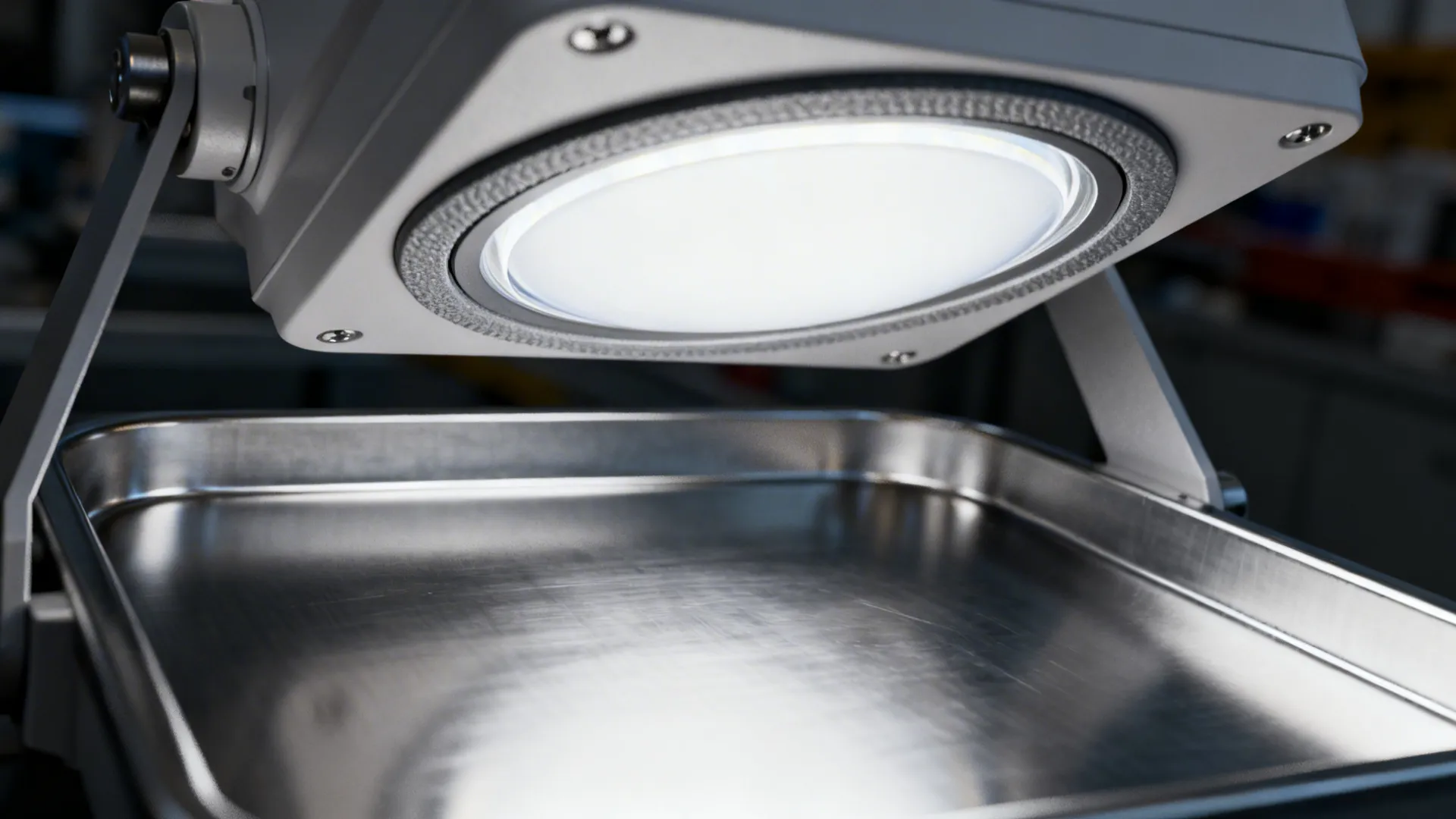 A bright round light fixture shines directly onto a clean metal tray in a dark room