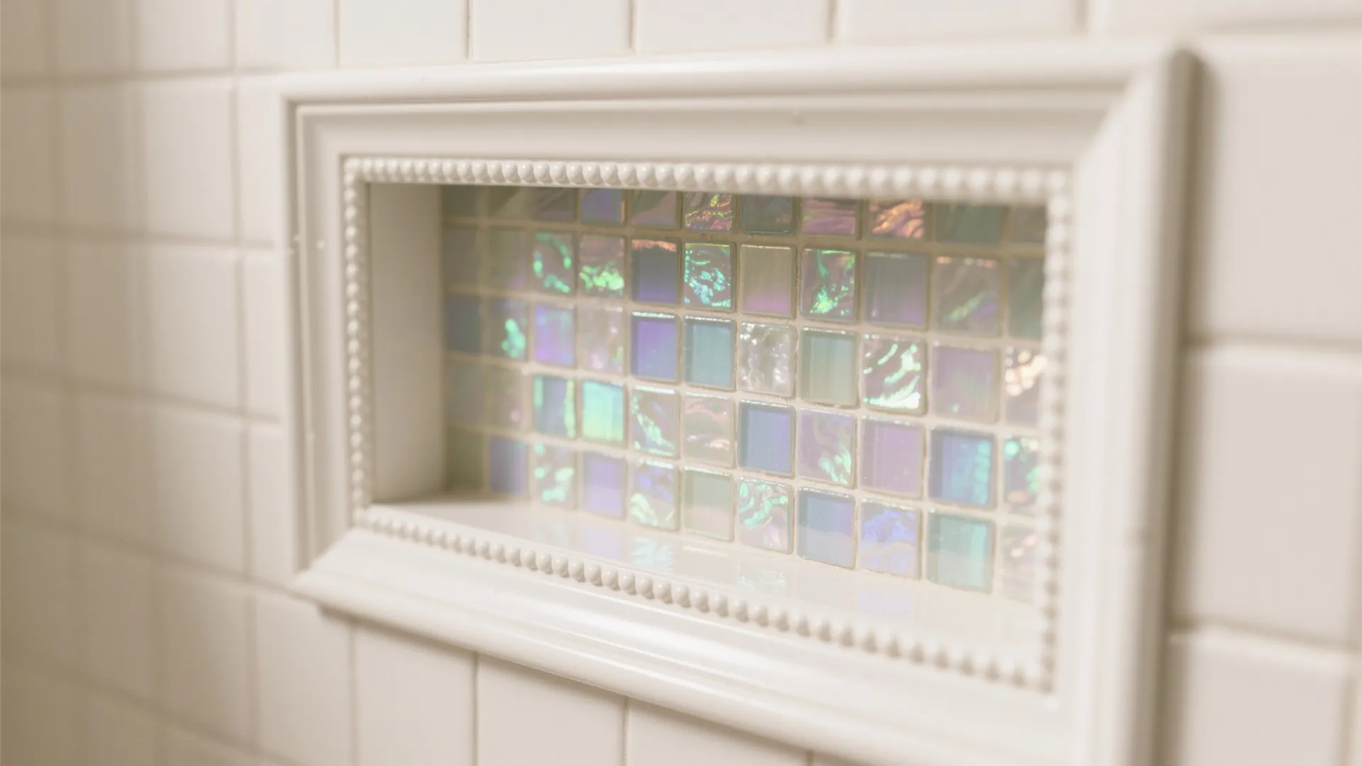 Close-up of a shower niche with iridescent glass mosaic framed by satin white tile.