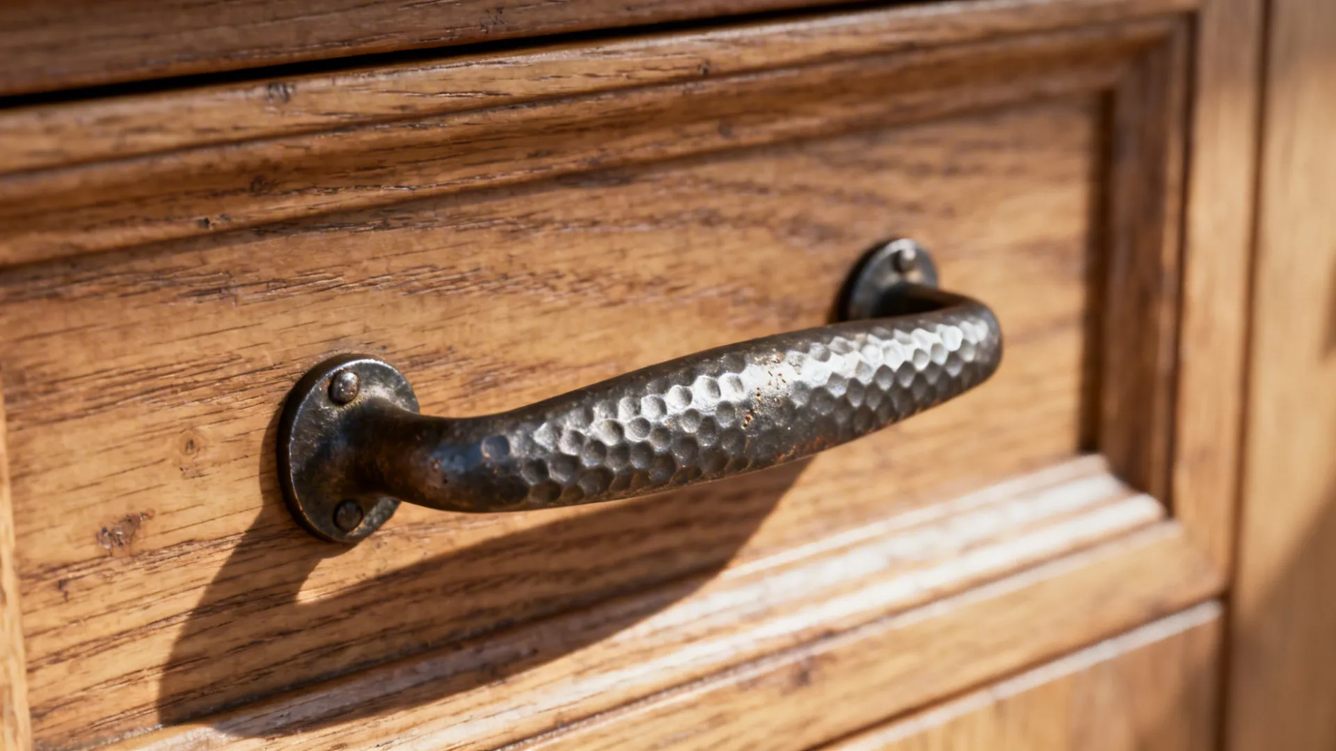 Macro detail of a forged iron pull on wire-brushed oak showing hammered texture.