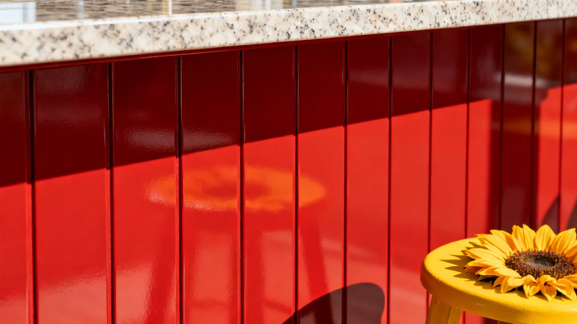 Macro of tomato-red island corner with quartz overhang and a yellow stool nearby.