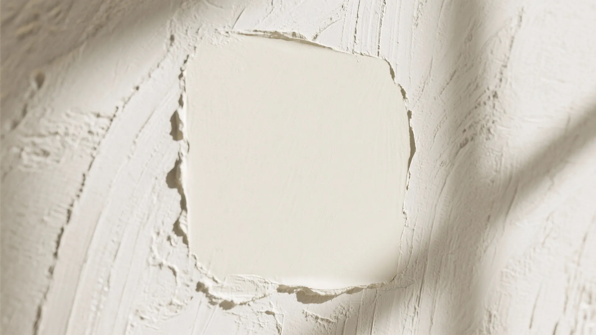 Rough ivory plaster wall texture featuring a smooth central square under soft natural light and shadows