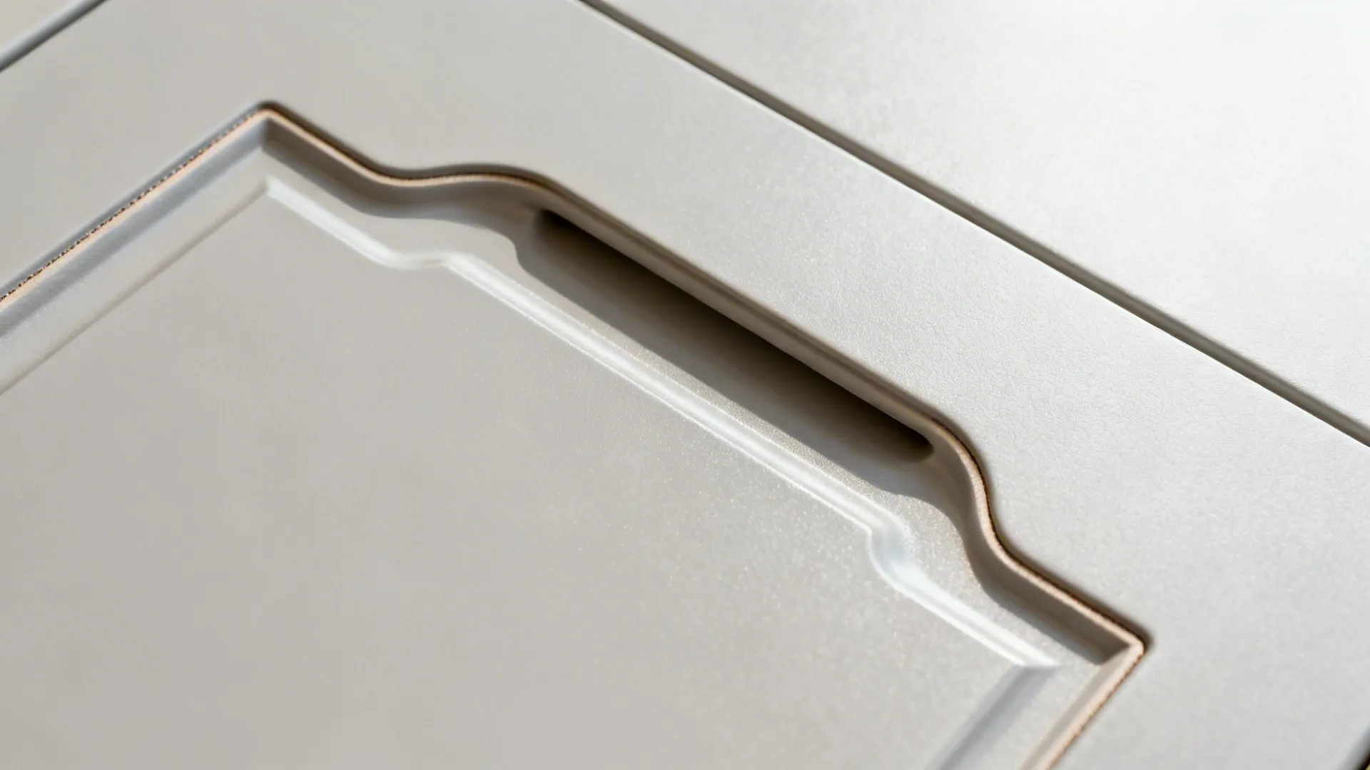 Close up of white kitchen cabinet door showing integrated handle detail and decorative wall panel texture