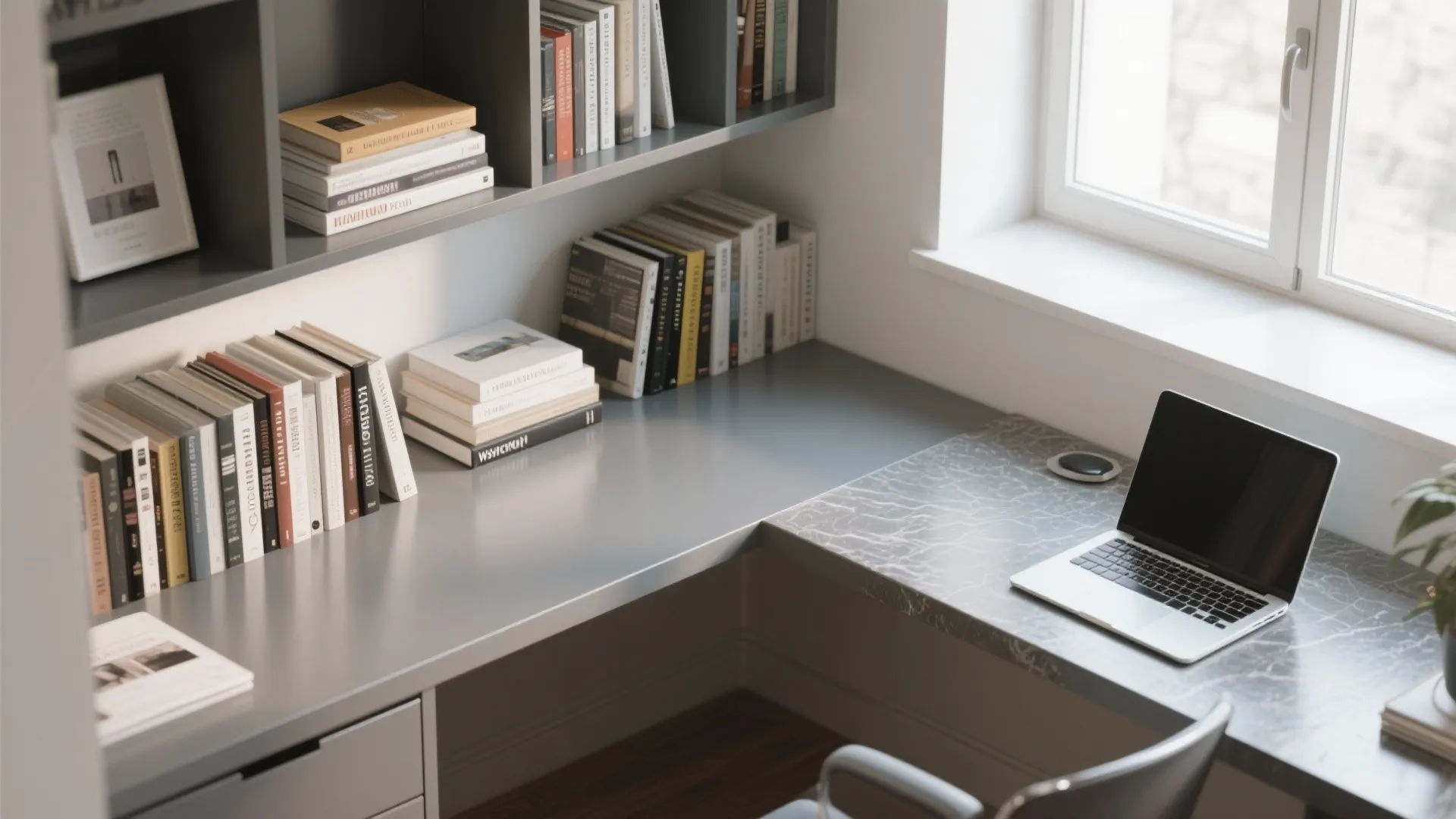 Grey corner desk with laptop many books on shelves marble table surface and bright room window