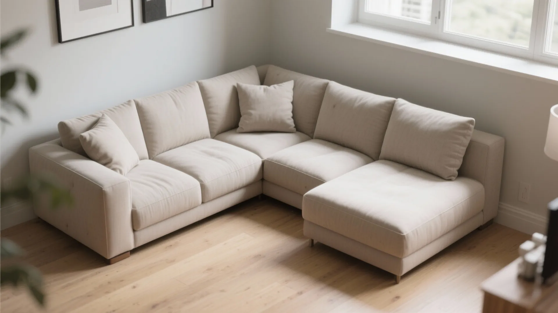 Beige l shaped sofa in corner of living room with wood flooring and natural light