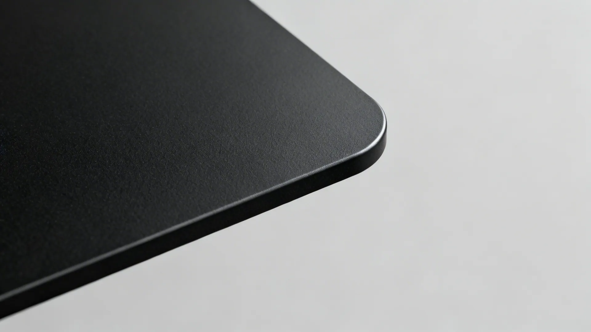 Smooth matte black rounded corner of a modern furniture piece against a plain light grey background