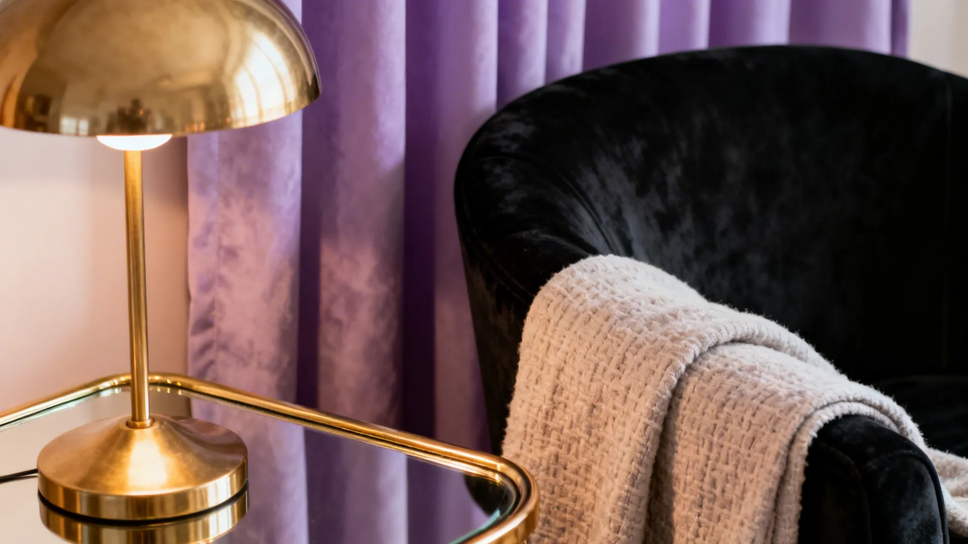Black velvet armchair next to lavender curtains with a warm brass lamp highlighting textures.