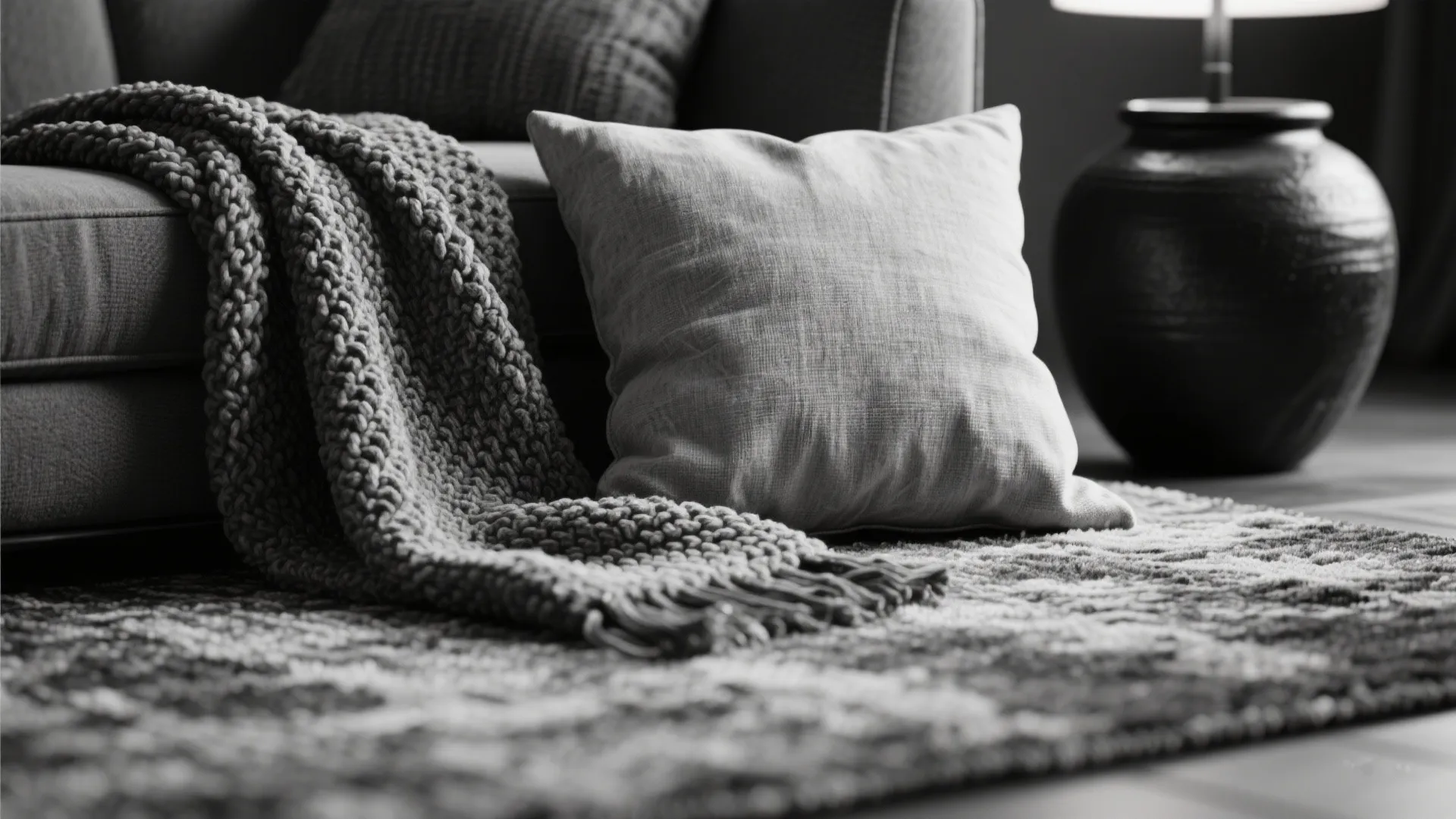 Close up of soft grey pillow and knitted blanket on a rug near a sofa