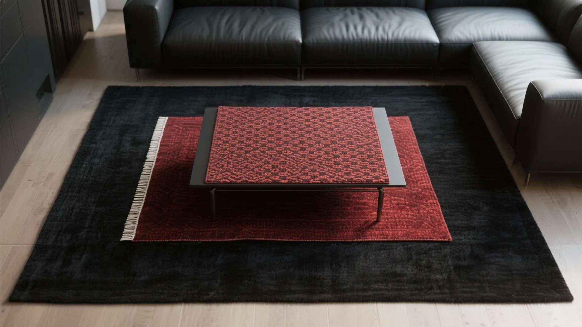 Top-down of layered rugs: a large black base rug with a smaller patterned red rug centered under a sofa.