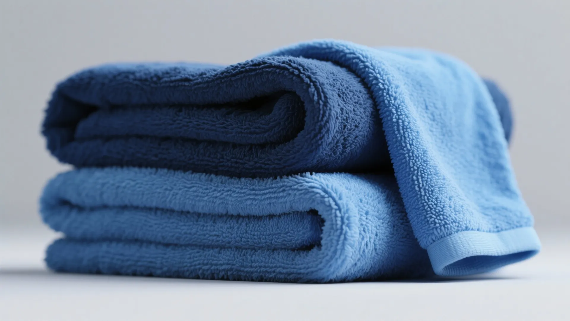 Soft folded blue cotton towels stacked neatly on a white surface with a clean background