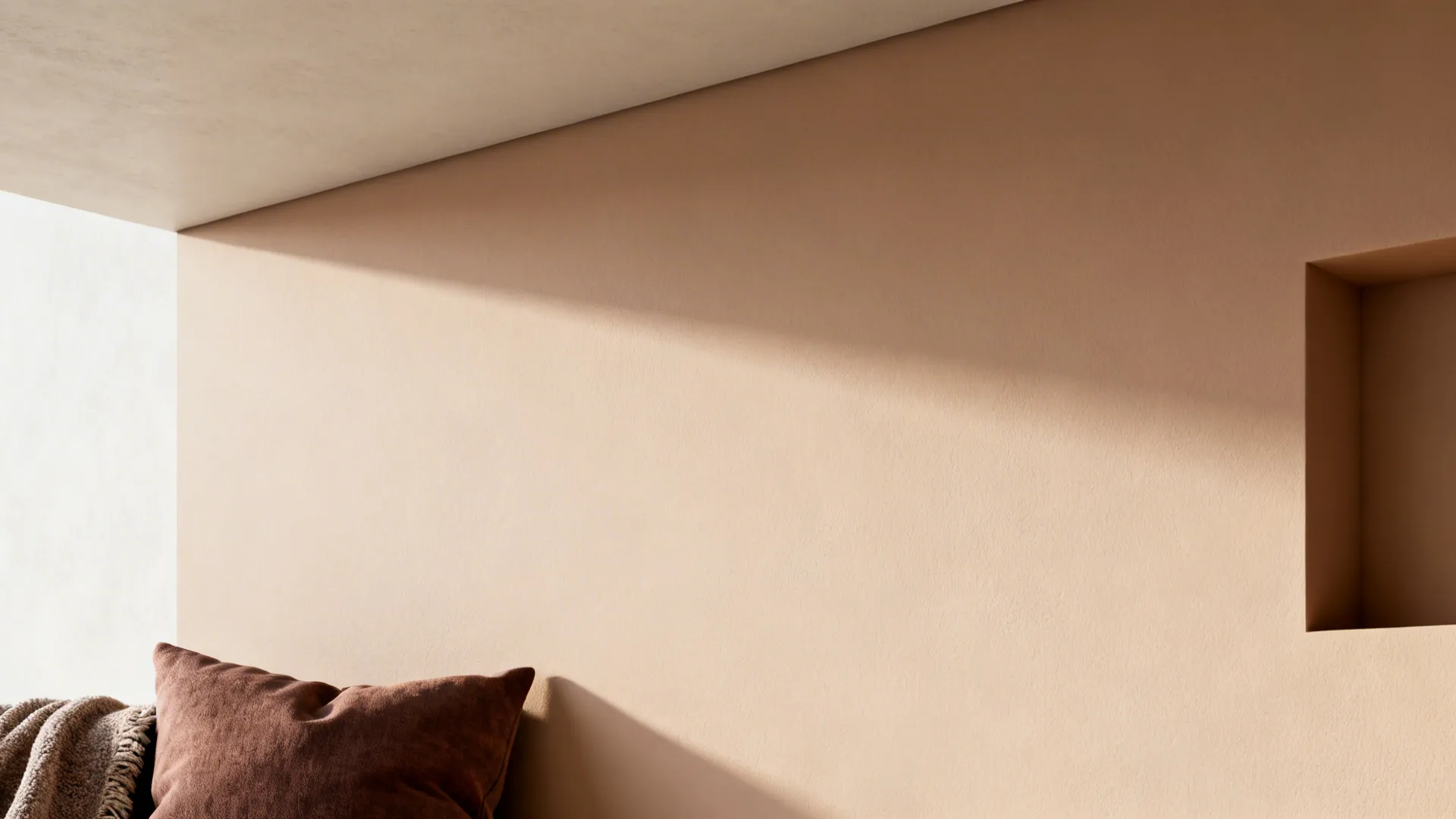 Wall and ceiling with pale warm neutral paint and a slightly darker accent textile in soft daylight