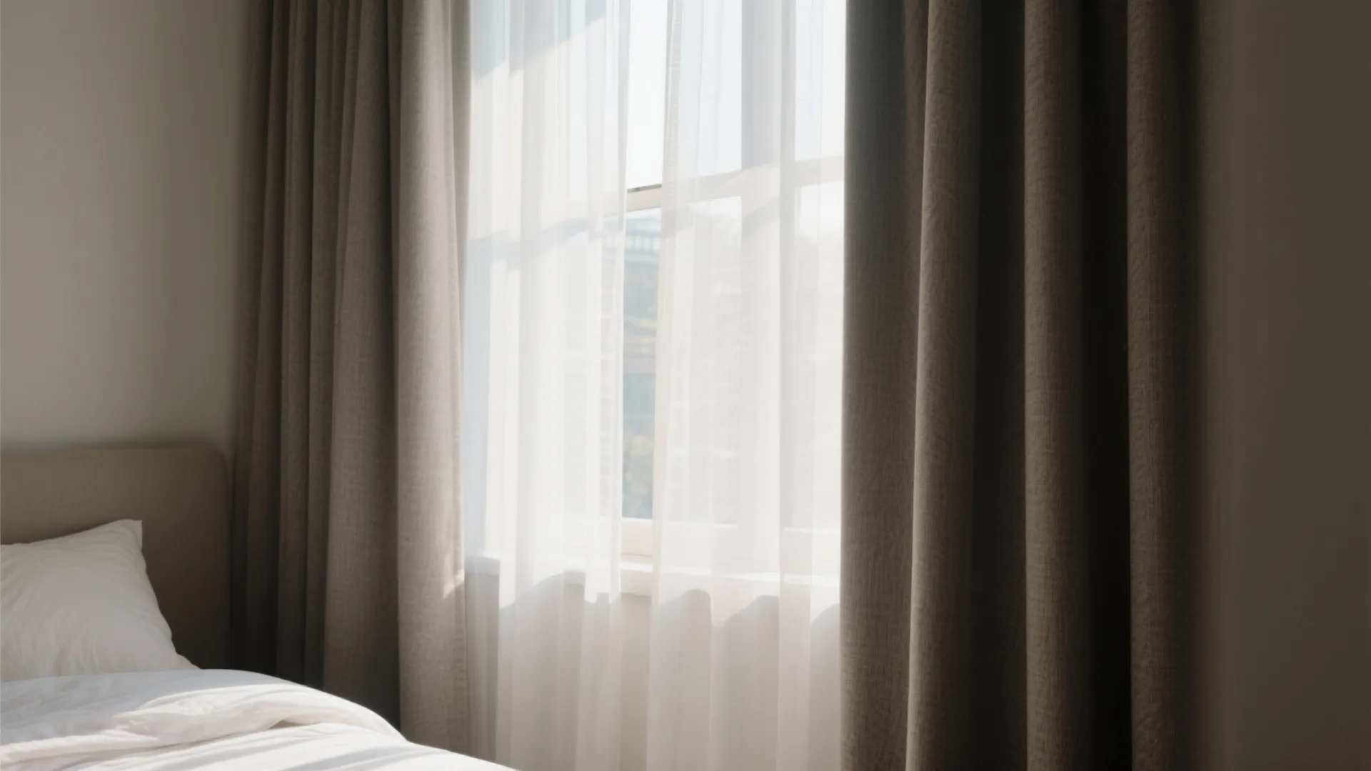 Modern bedroom window with brown curtains and white sheer fabric letting in bright natural sunlight