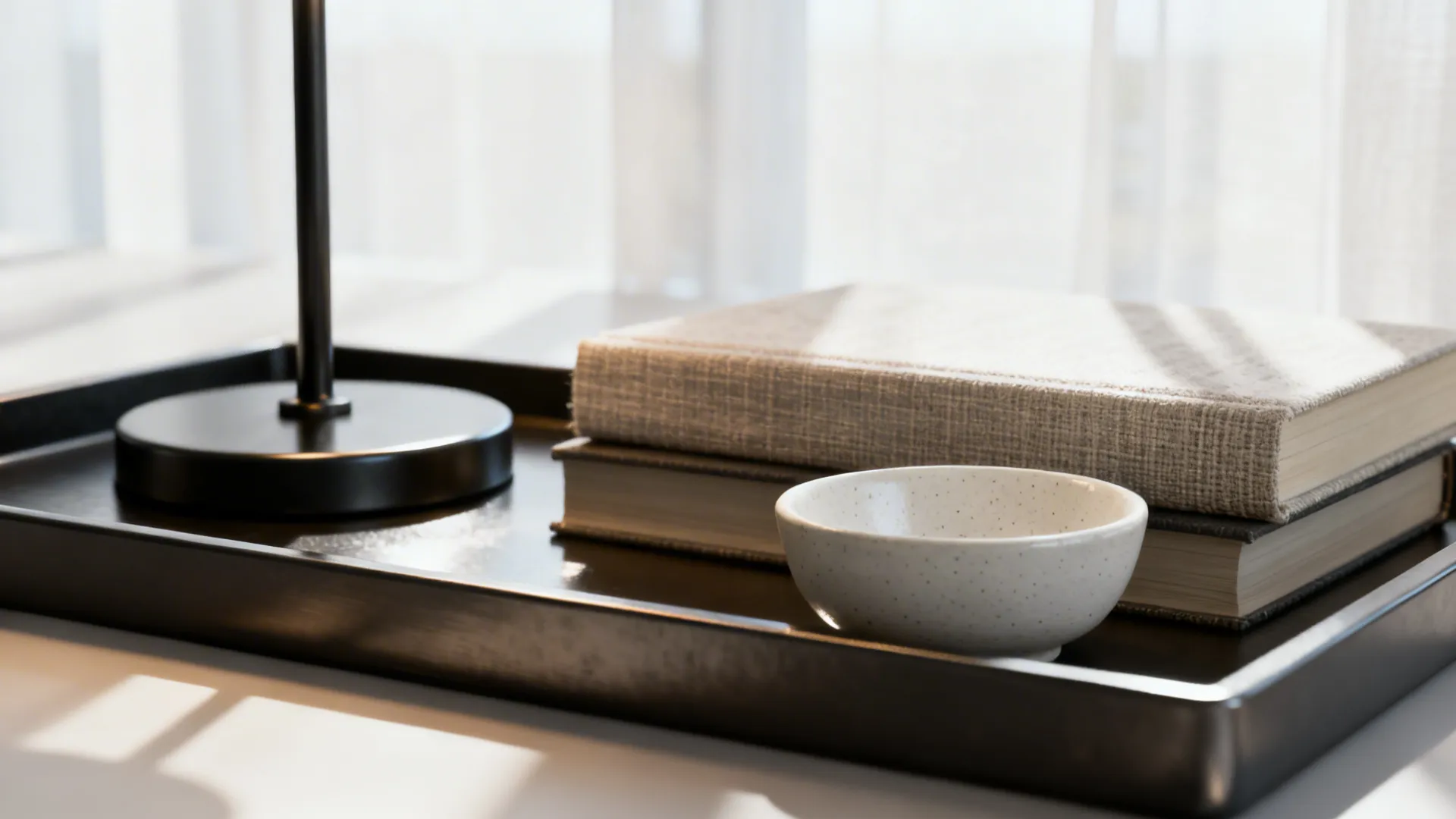 Close-up of tray with lamp, stacked books, and ceramic bowl on an end table