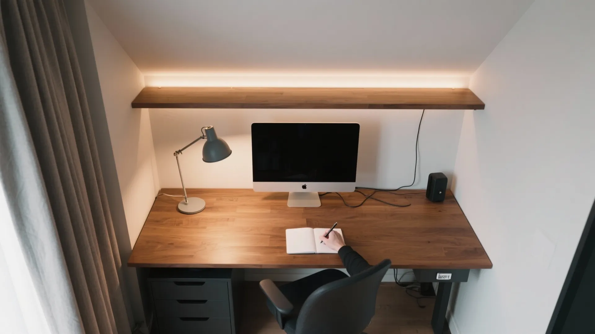 Modern home office with wood desk, black monitor, desk lamp, and overhead warm strip light