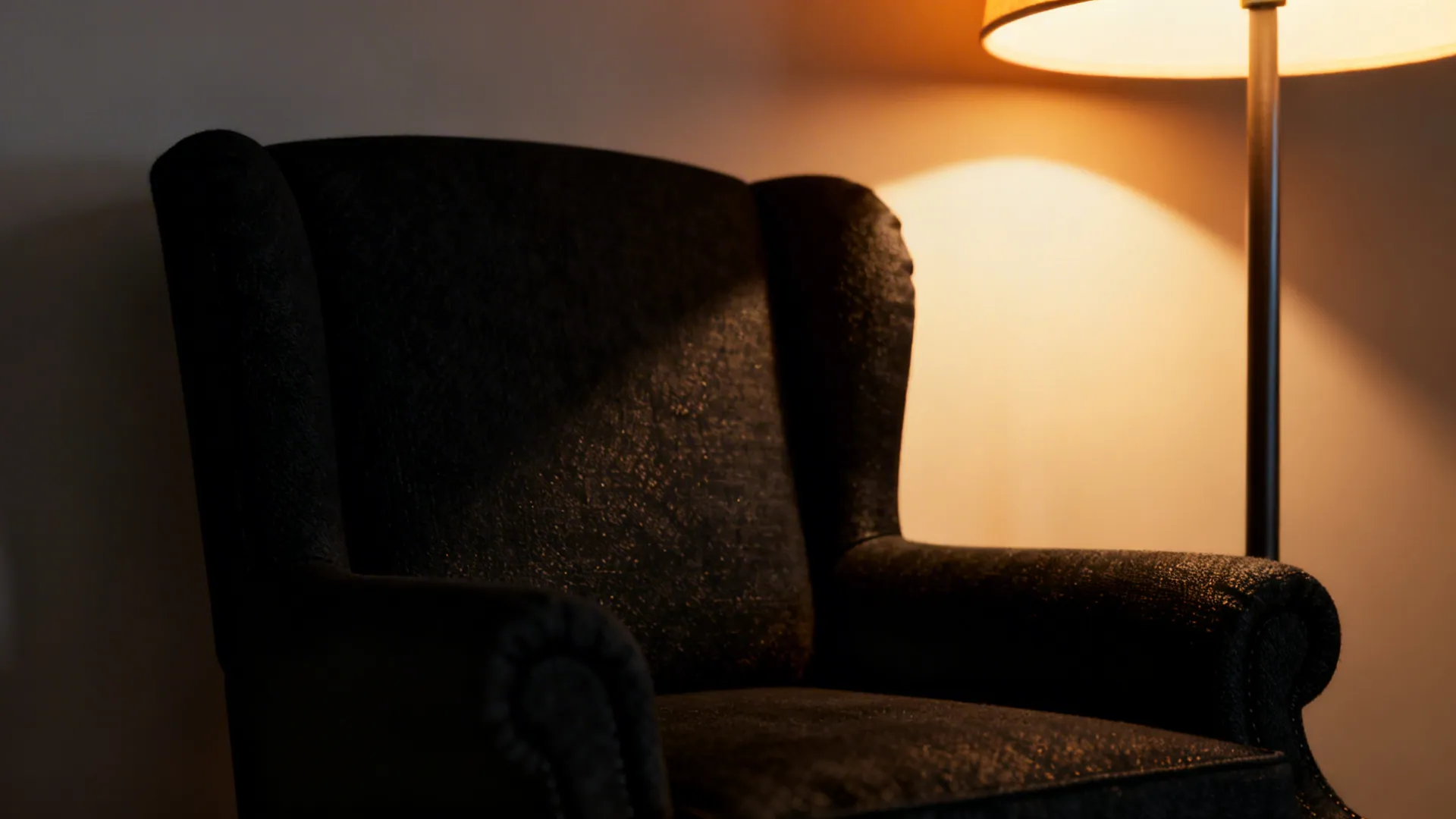 Warm floor lamp and uplighter softening a black armchair in a cozy living room