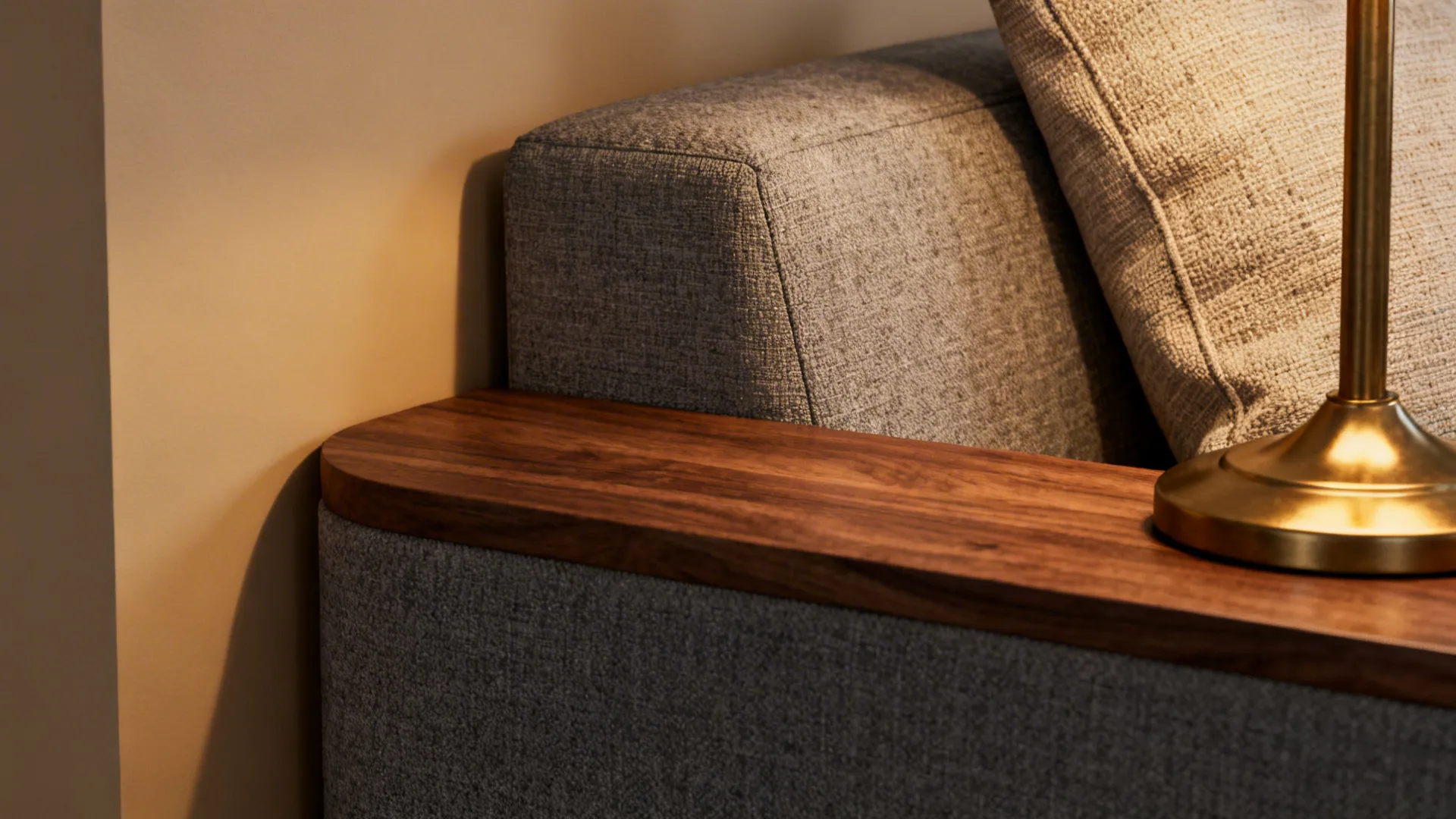 Close-up of beige wall, grey sofa fabric, walnut table edge and brass lamp showing texture contrast.