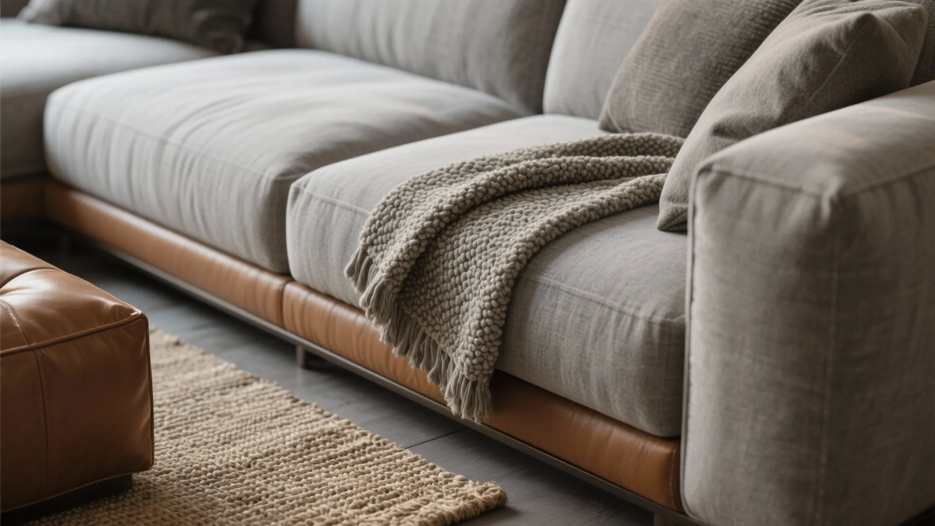 Close view of a grey fabric sofa with leather trim a knitted blanket and rug
