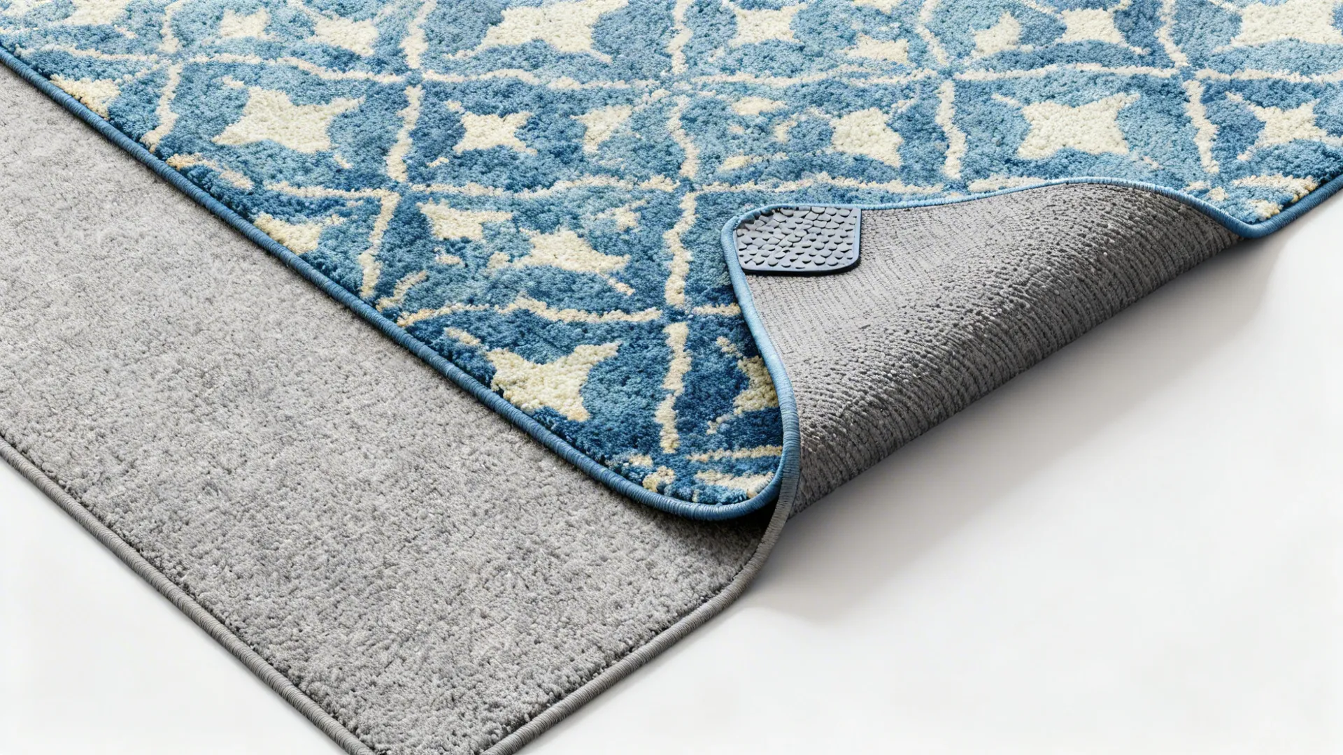 Top-down view of a neutral grey rug layered with a smaller patterned blue rug and a visible non-slip pad.