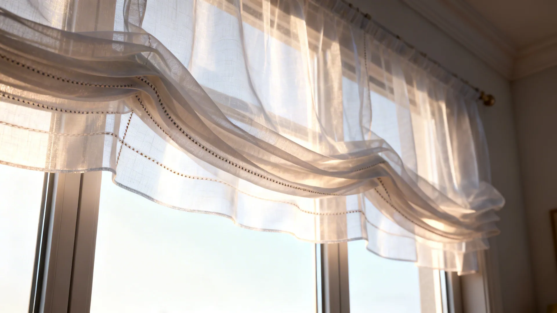 Close-up of layered sheer valances softly filtering daylight over a large window.