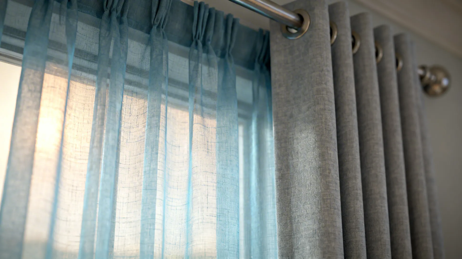 Close-up of soft blue sheer layered over a dove-grey blackout curtain showing fabric texture and light diffusion.