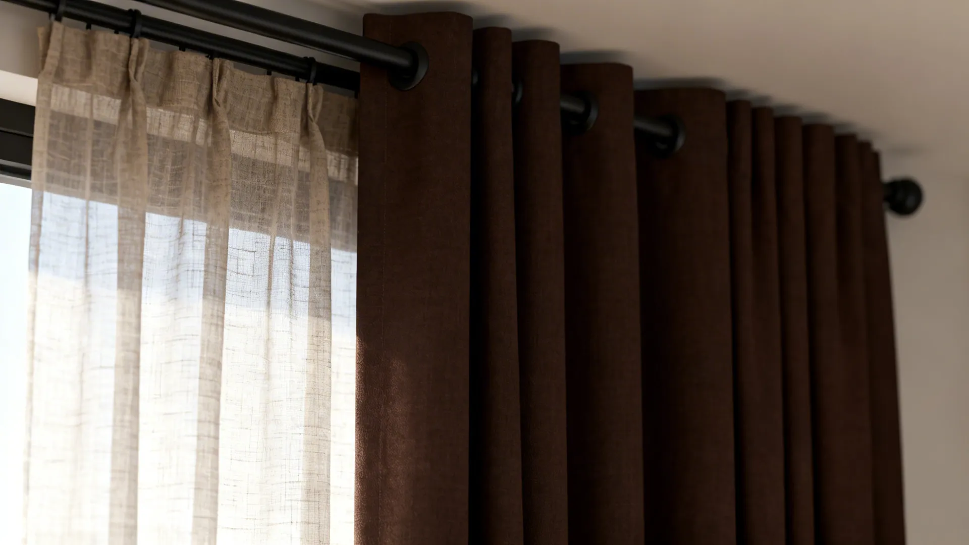 Dark brown curtains paired with light sheer fabric hanging on a black metal curtain rod